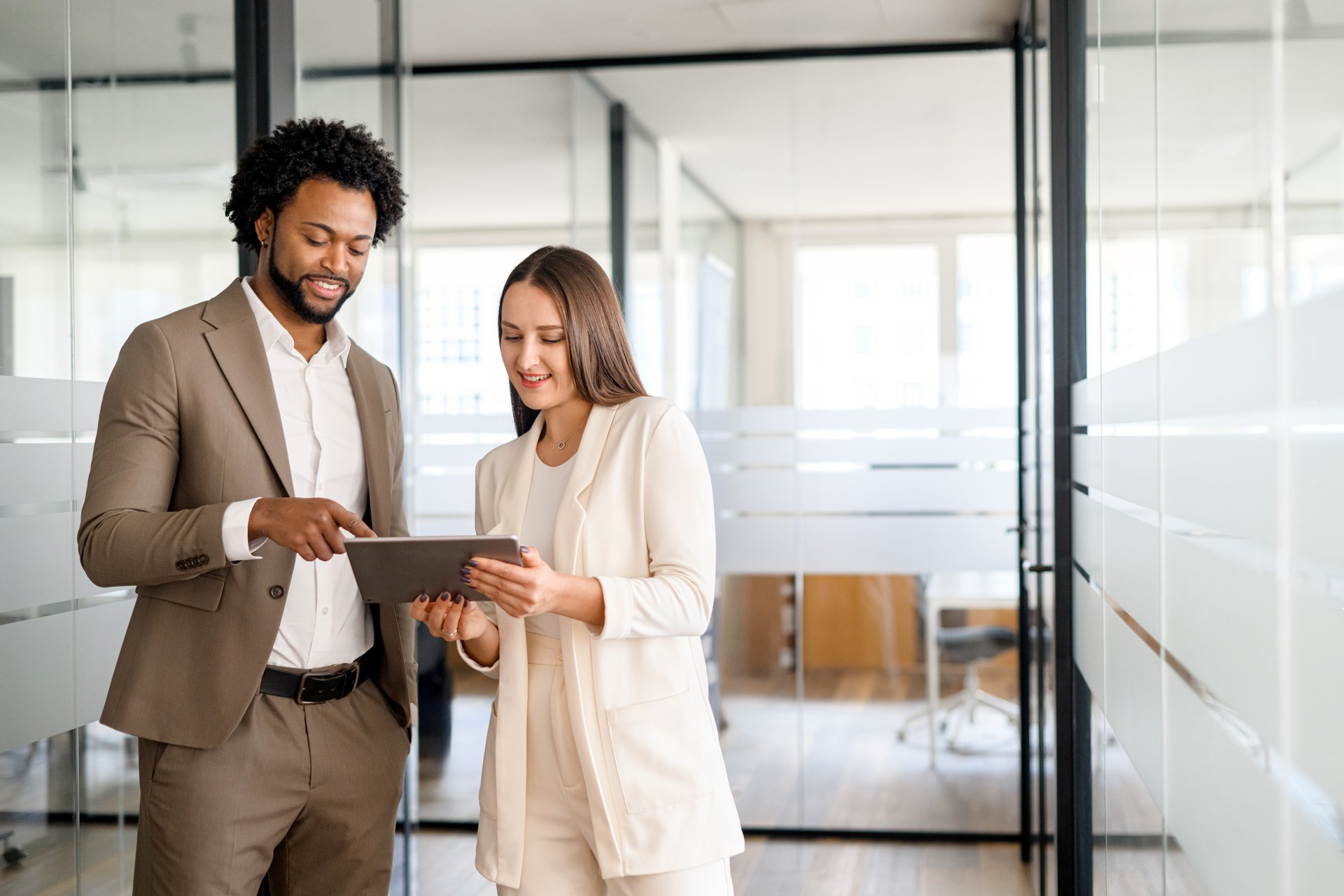 African-American businessman and his colleague watching at tablet screen, engaged in constructive business dialogue. The open office setting provides an atmosphere of transparency and forward-thinking