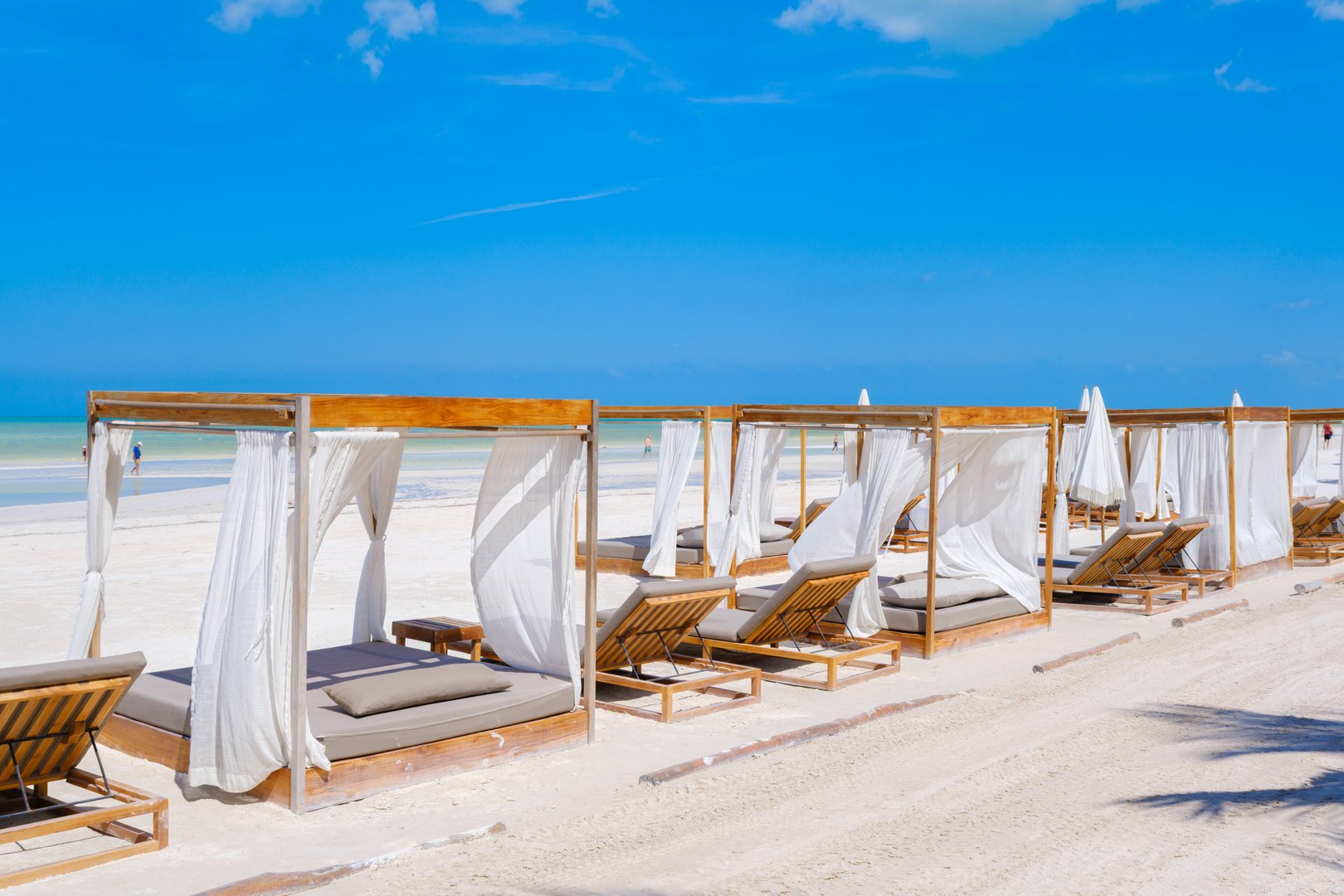 Elegant wooden beach cabanas with white curtains face the turquoise Caribbean Sea on the pristine sands of Isla Holbox.