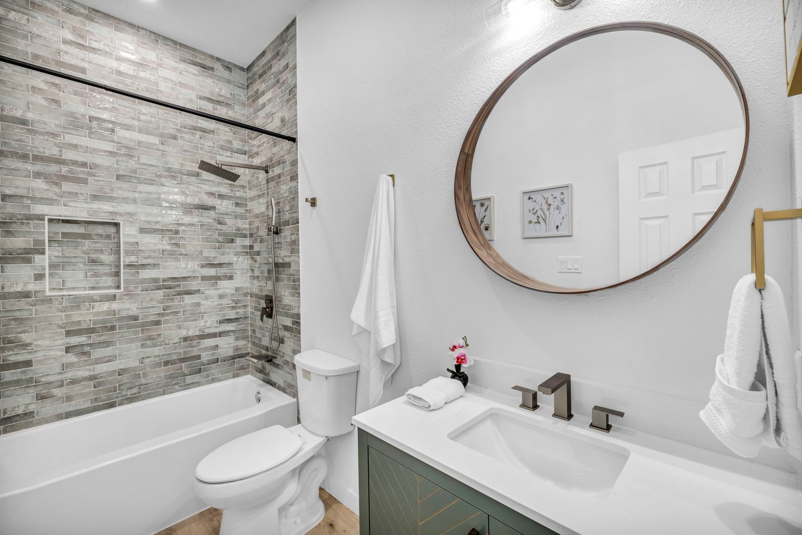 Modern bathroom with circular mirror, white sink, green cabinet, and tiled shower with glass door.