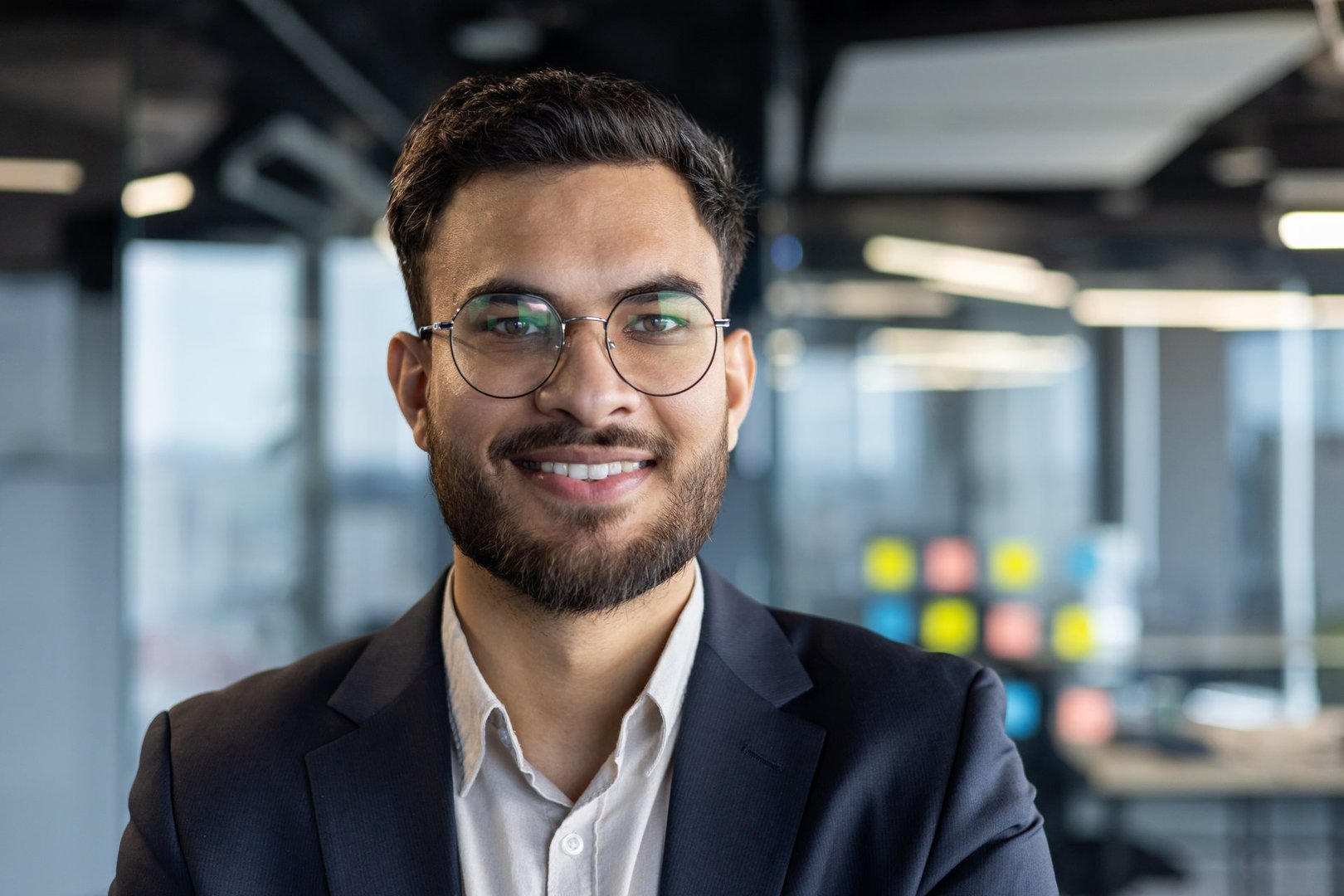Portrait of successful businessman inside office. Man in business suit smiling and looking at camera close up. Satisfied banker investor in glasses at workplace.
