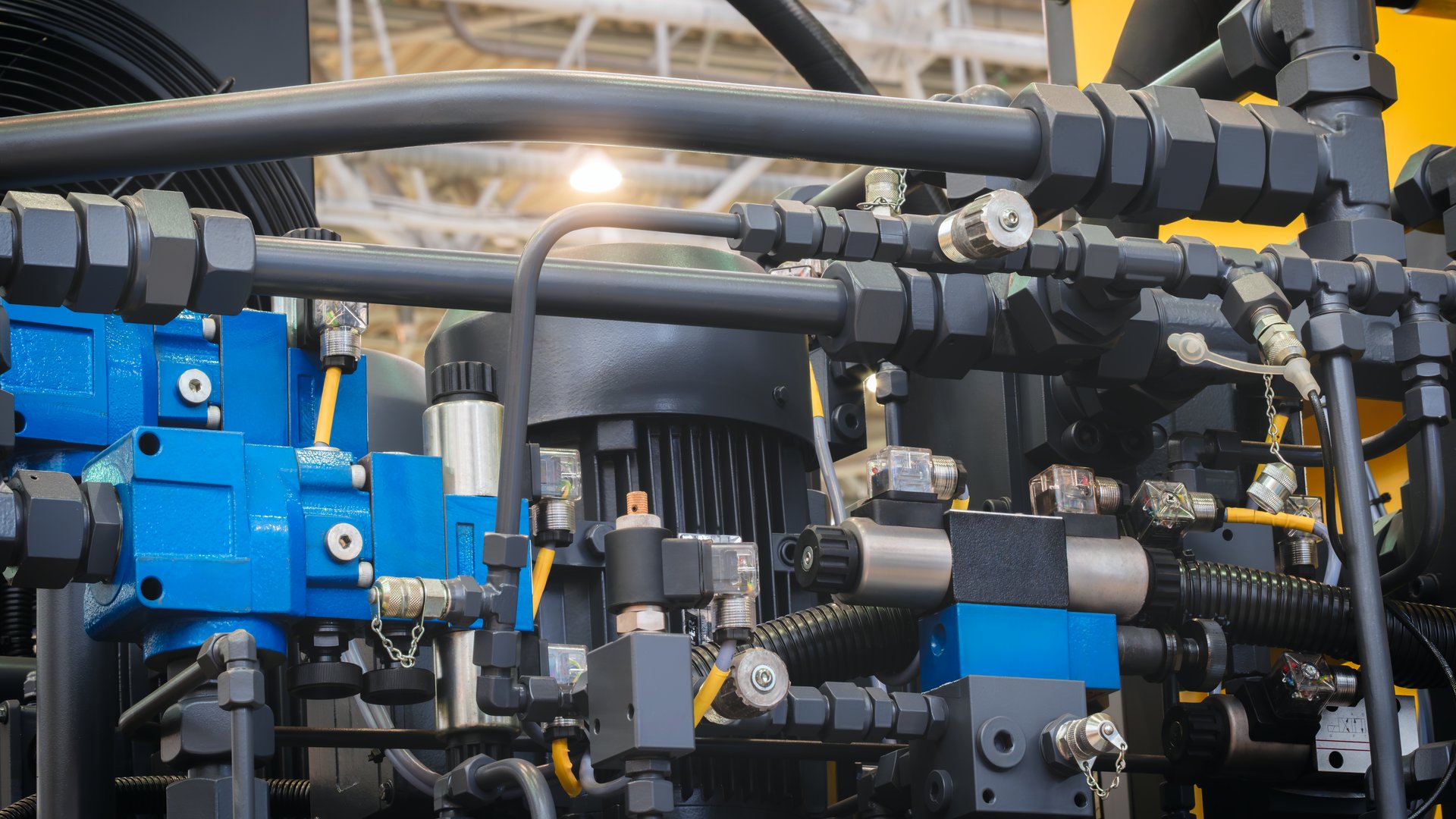 A machine with many pipes and valves. The valves are blue and yellow. The machine is in a factory