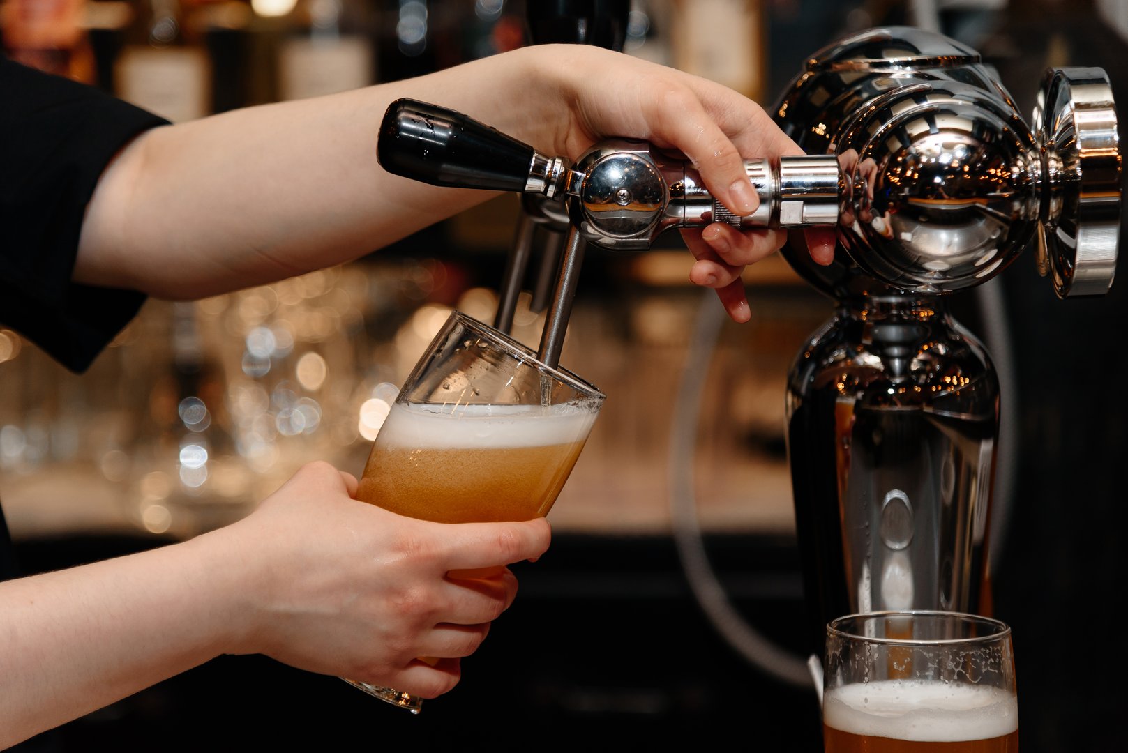 bartender pours light beer into large beer mug for customer at bar, close-up view of hand holding mug
