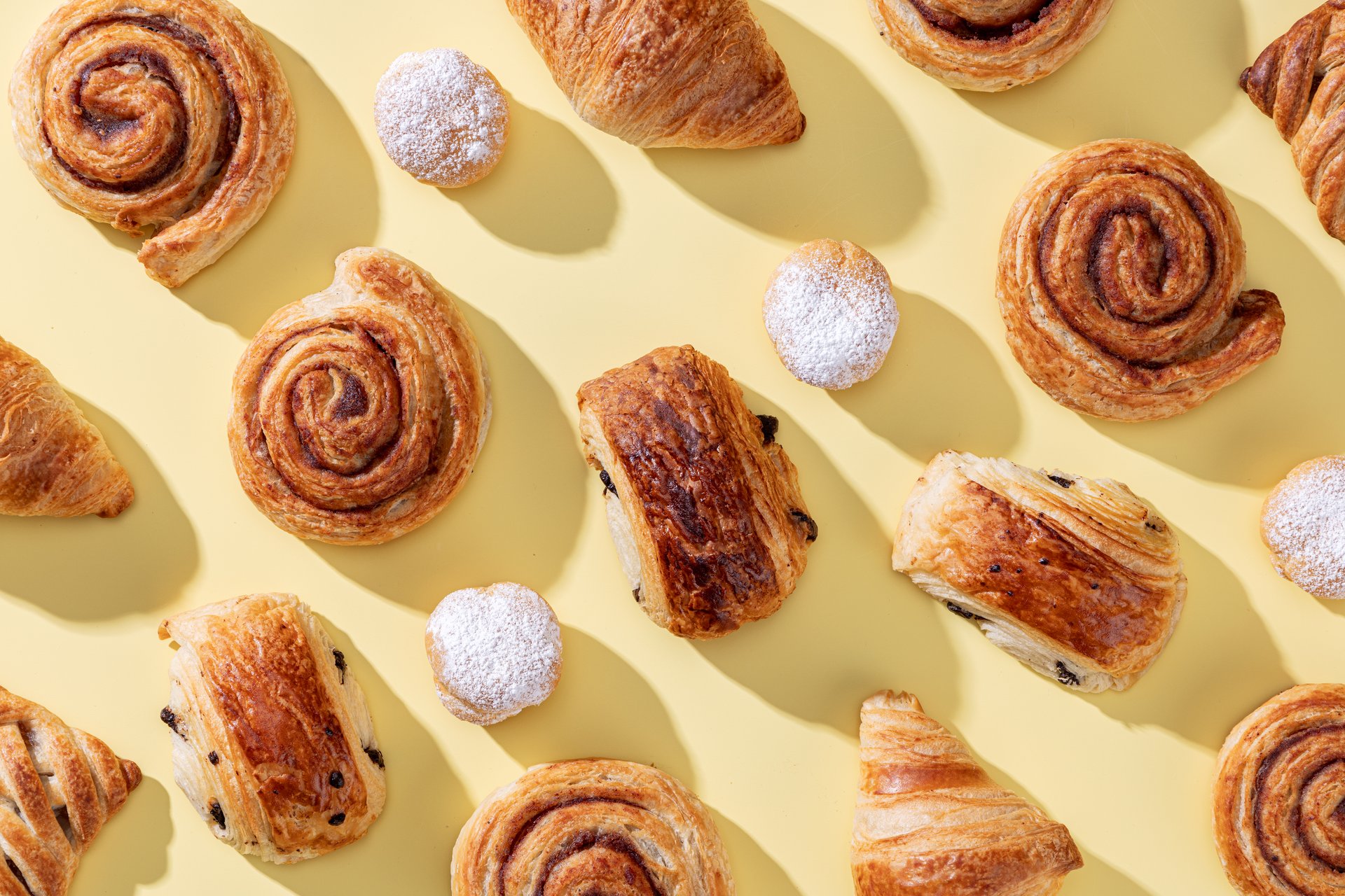 various freshly baked pastries on light yellow background, top view