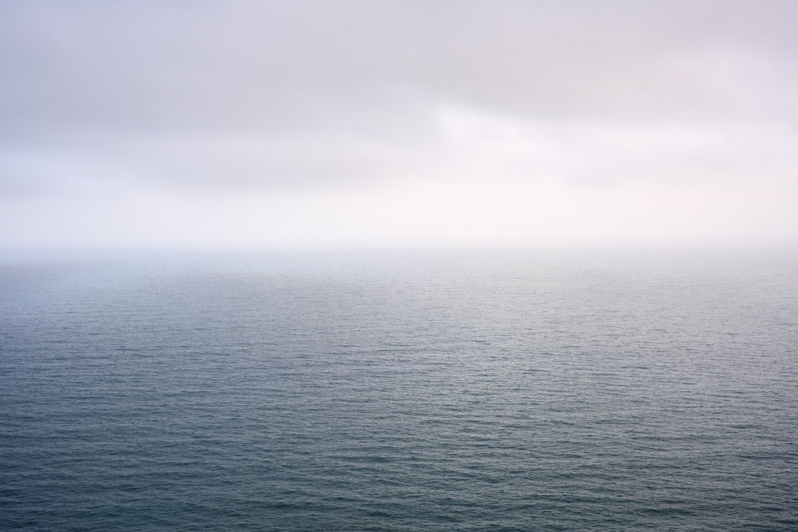 Calm ocean landscape under cloudy sky: minimalist seascape with overcast atmosphere.