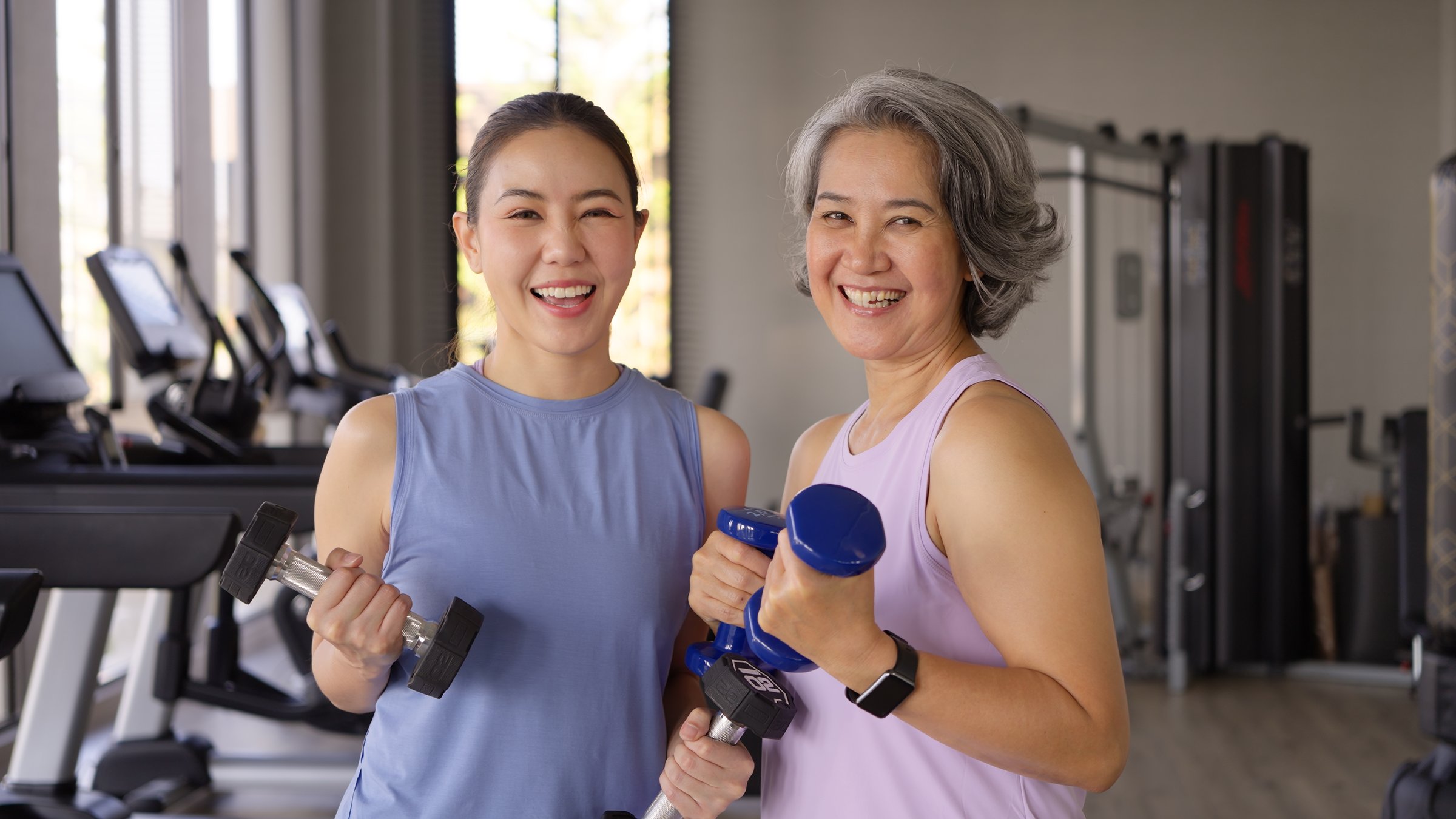 Young adult child and middle age old mum smile look at camera gym workout body weight picking up arm lift dumbbell. Health care older mom asia elder people happy protect aging life sport build muscle.