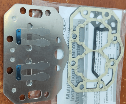 Two metallic and gasket components with manuals on a wooden surface, likely parts for machinery or automotive use.