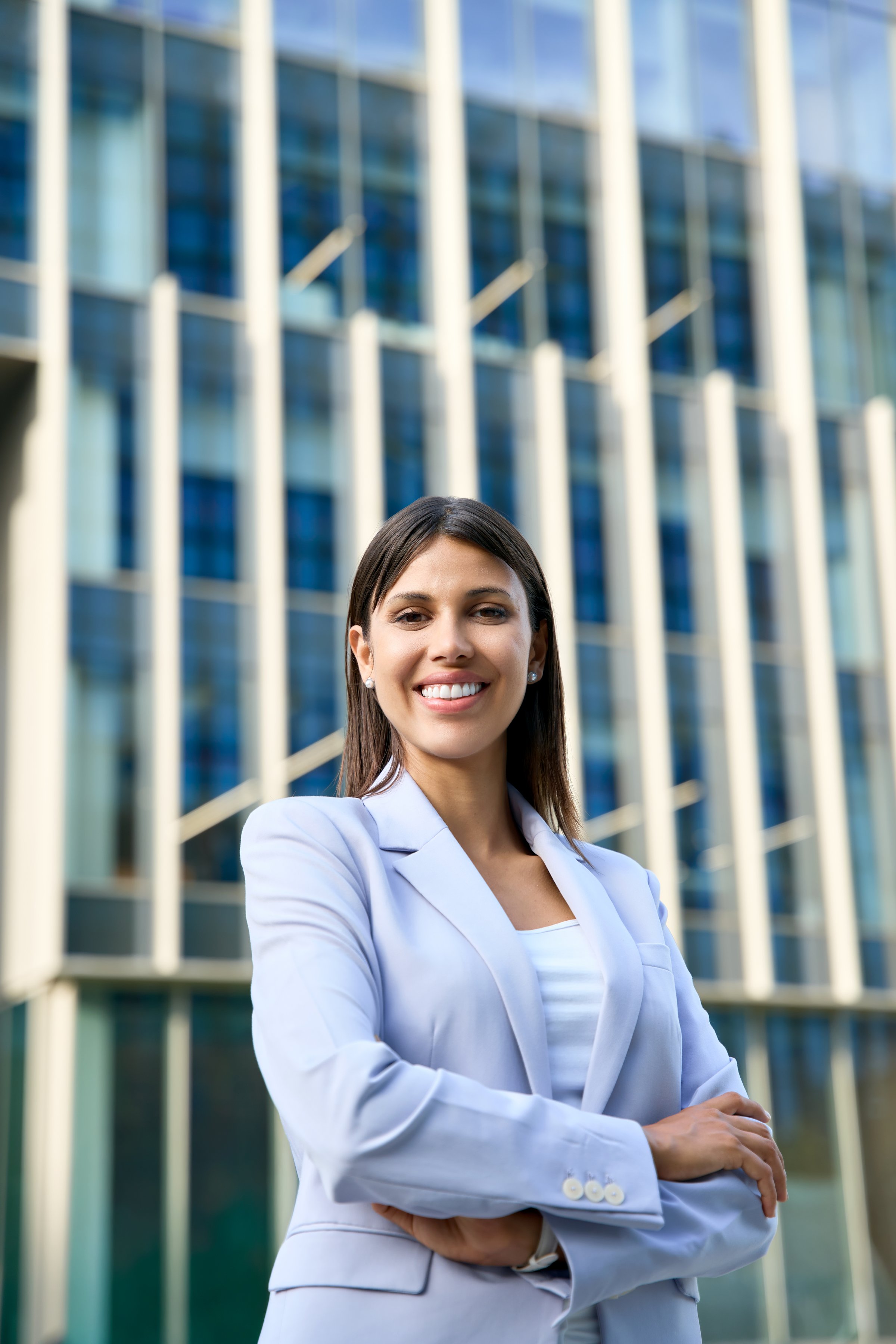 Vertical portrait of hispanic business woman with crossed arms smiling at camera outside. European or latin confident mature good looking middle age leader female businesswoman at office building