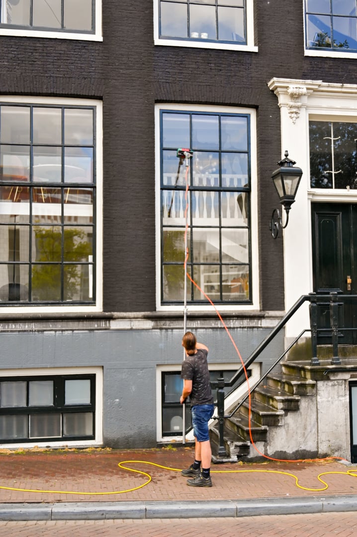 Amsterdam, Netherlands - August 2022:  Person cleaning the windows of a building using an extendable pole with a brush and hose