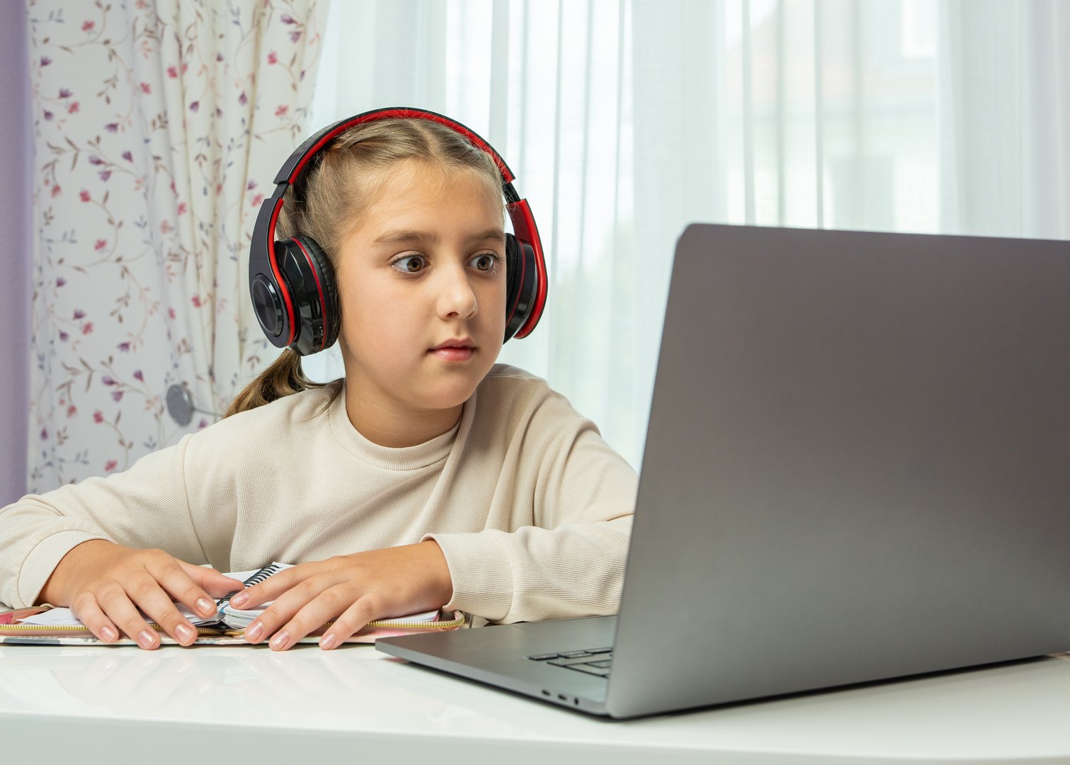 Child wearing headphones focused on laptop screen during home study session. Great for illustrating online education, remote learning, technology in modern childhood.