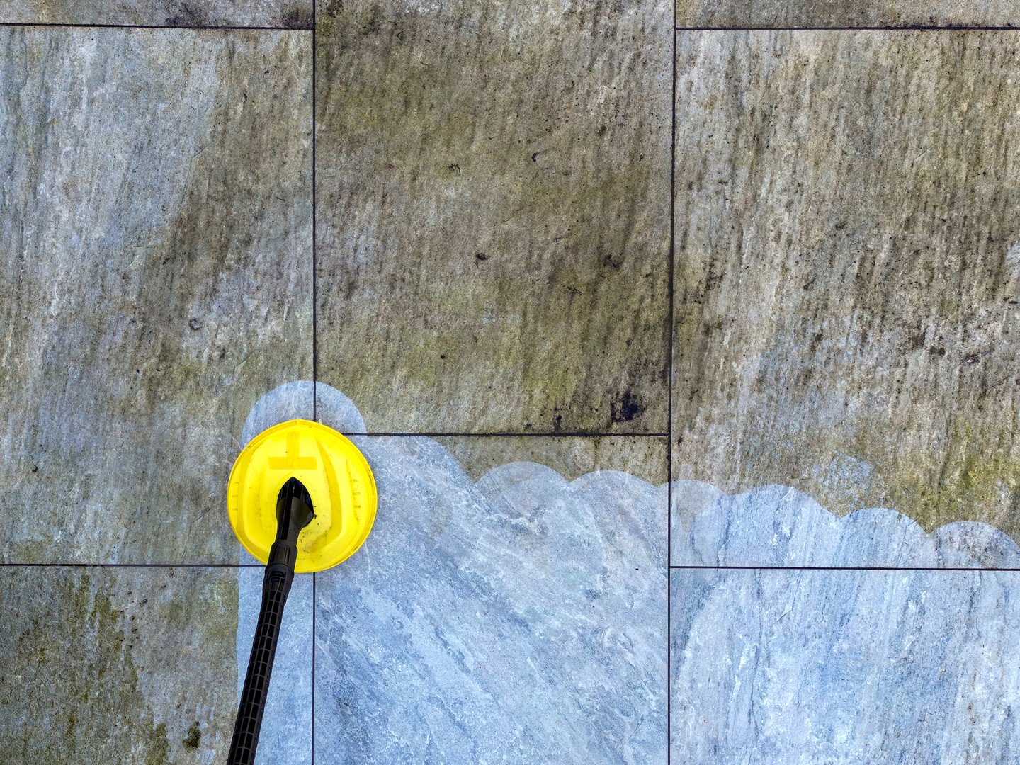 Pressure jet washer being used to clean porcelain tiles on a garden patio showing the difference before and after cleaning