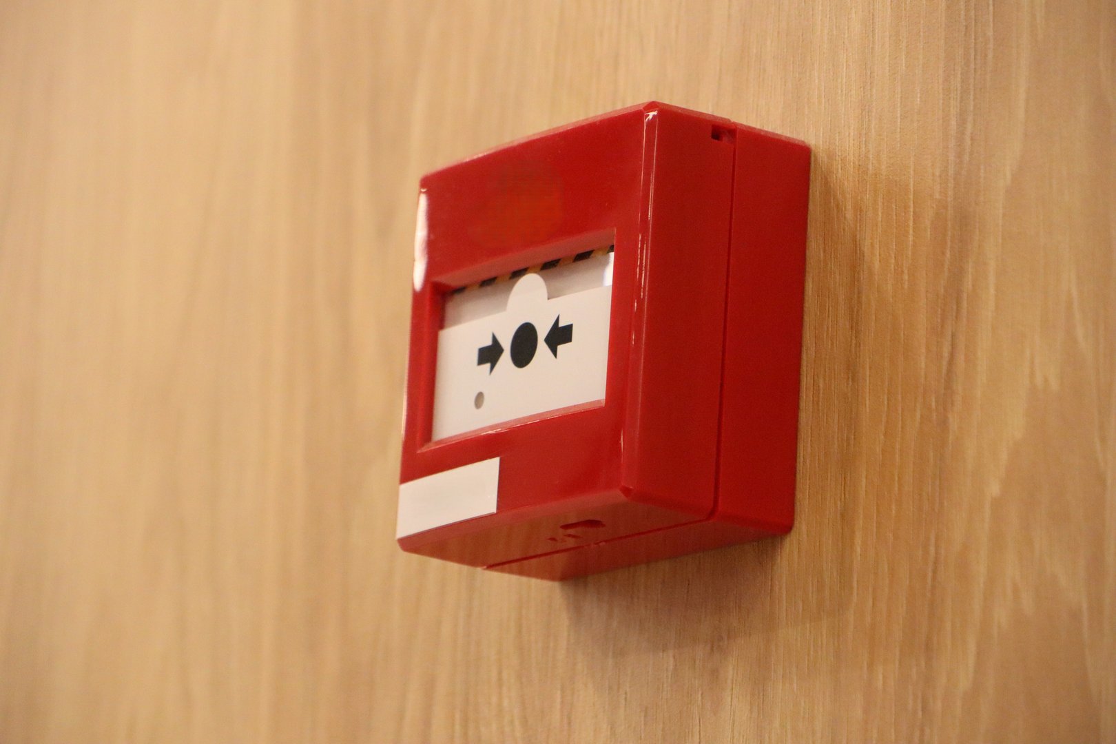 A bright red fire alarm call point that is strategically mounted on a wooden wall specifically for emergency use