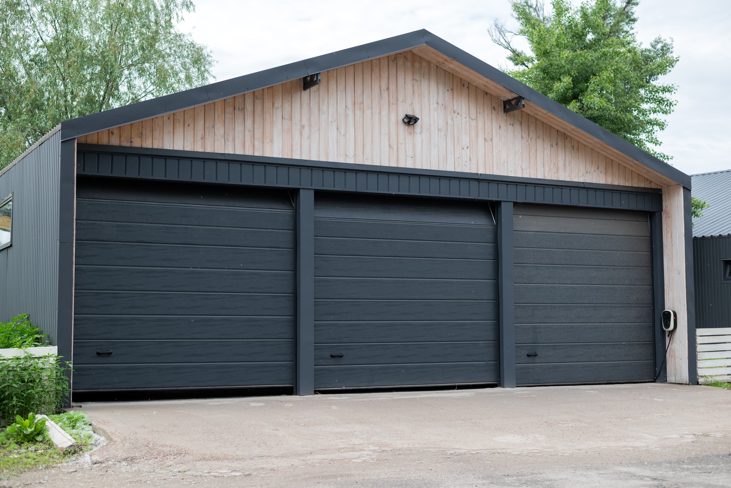 Modern three-door garage building with black automatic gates and light wood facade, located on a clean concrete driveway.