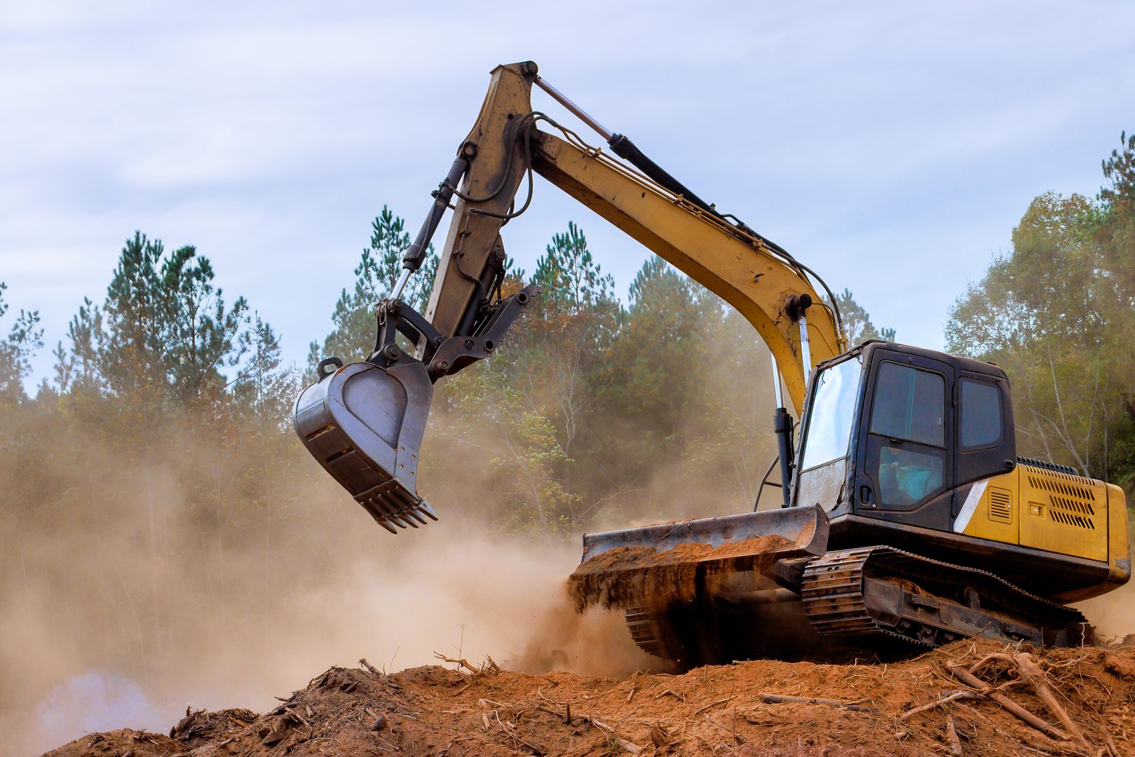 Heavy machinery is clearing trees dirt at construction site in forest, creating large dust cloud.
