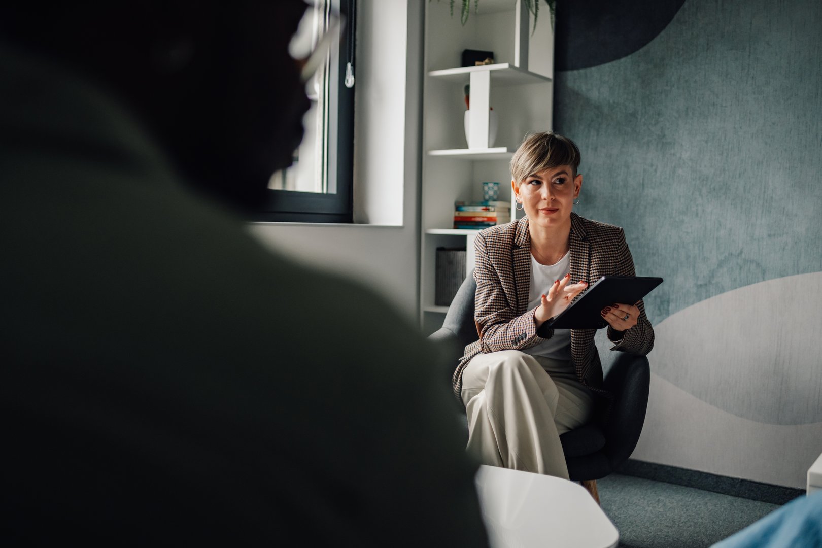 Psychologist engaging with her patient during a therapy session, presenting information on a digital tablet in a modern office setting, fostering communication and trust