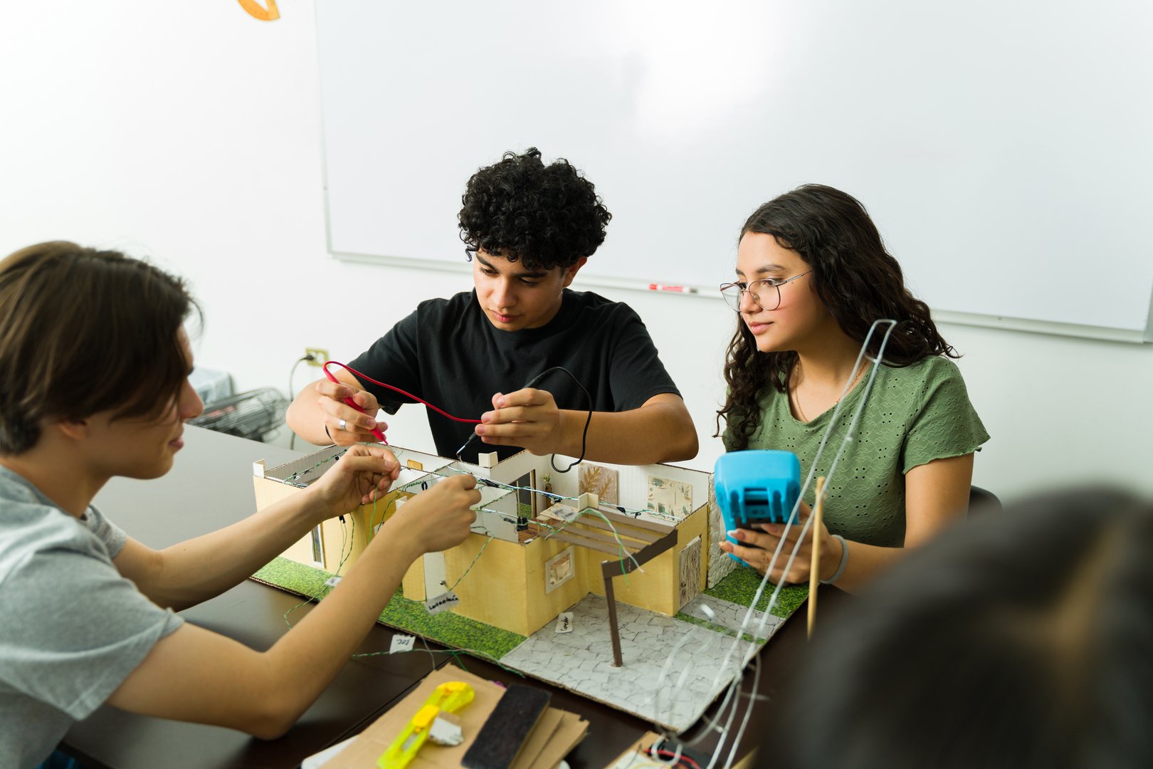 Latin american high school students working together on a science project involving electronics and a model house during a stem class