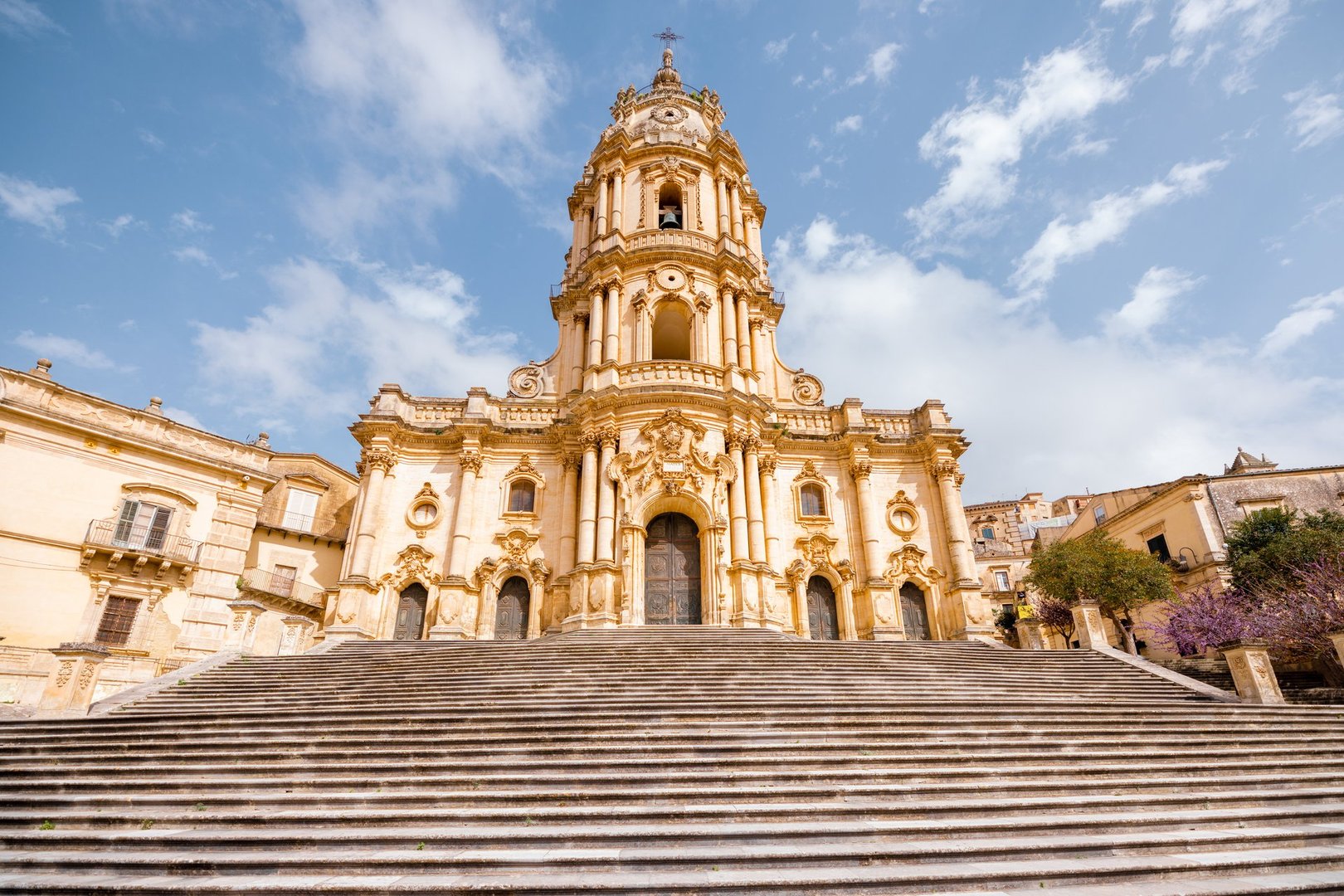 Majestic Baroque façade of the Cathedral of San Giorgio in Modica, Sicily, captured from the bottom of the grand staircase under a bright sky