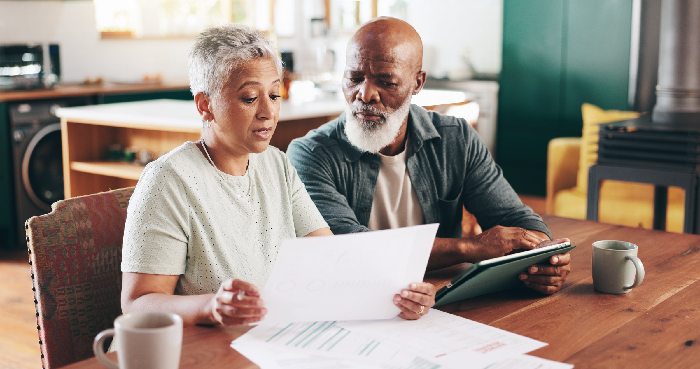 Mature, interracial couple and documents with tablet for financial discussion, planning or expenses at home. Man, woman or mortgage with paperwork or technology for payment due, finance or bills