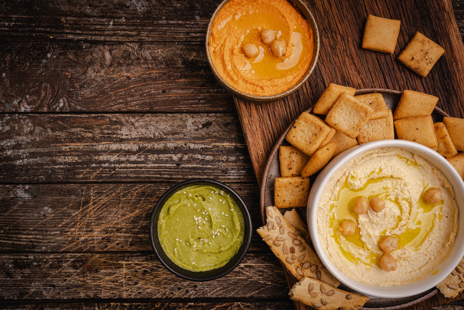 Various hummus dips in different colours. Hummus with dry crackers, top view. Vegan and traditional hummus as healthy and vegan snack.