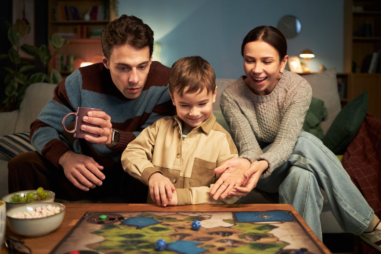Happy family playing board game together with little son at table in the room