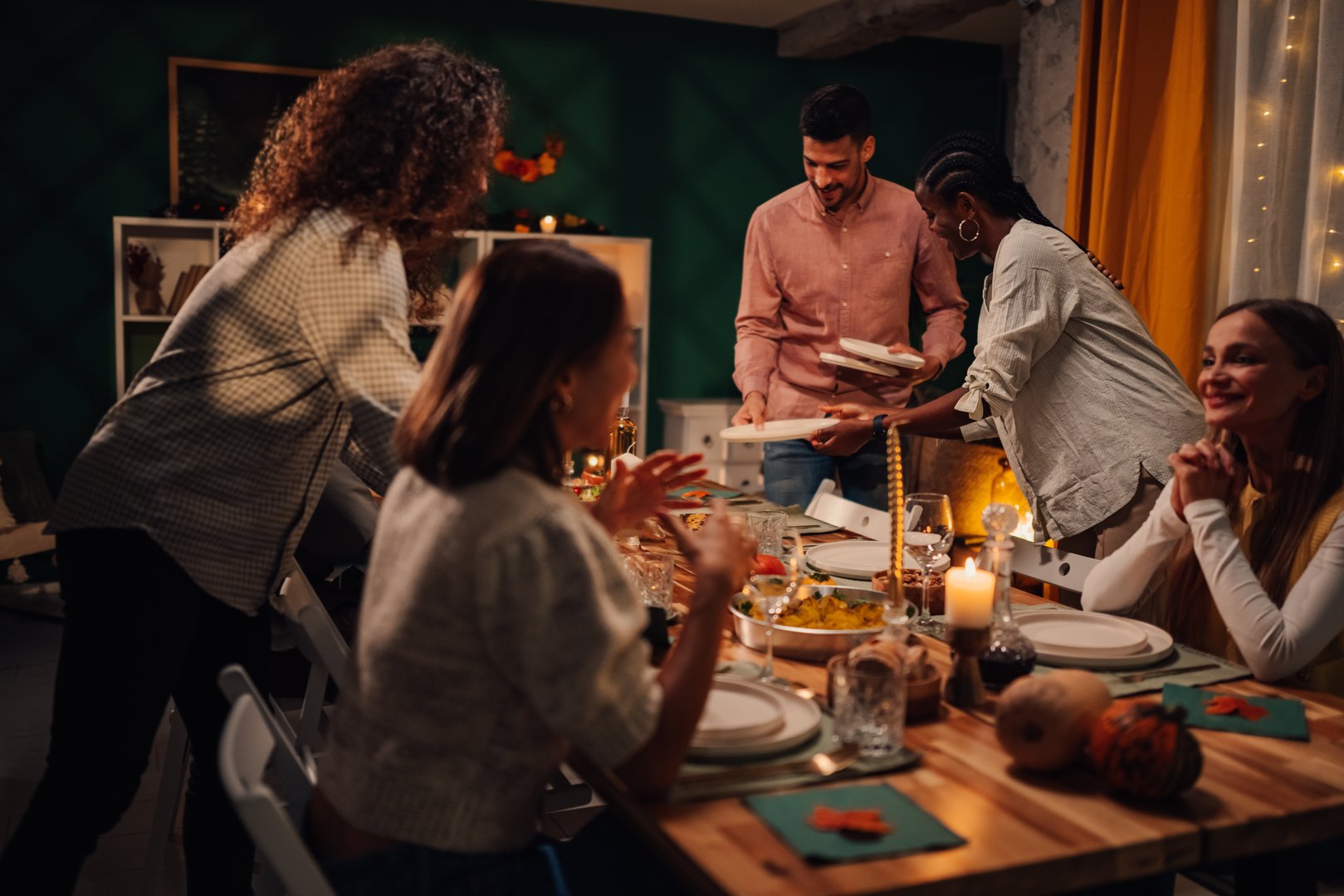 Friends joyfully setting the table for a thanksgiving dinner, arranging plates and sharing smiles in a warm, cozy atmosphere