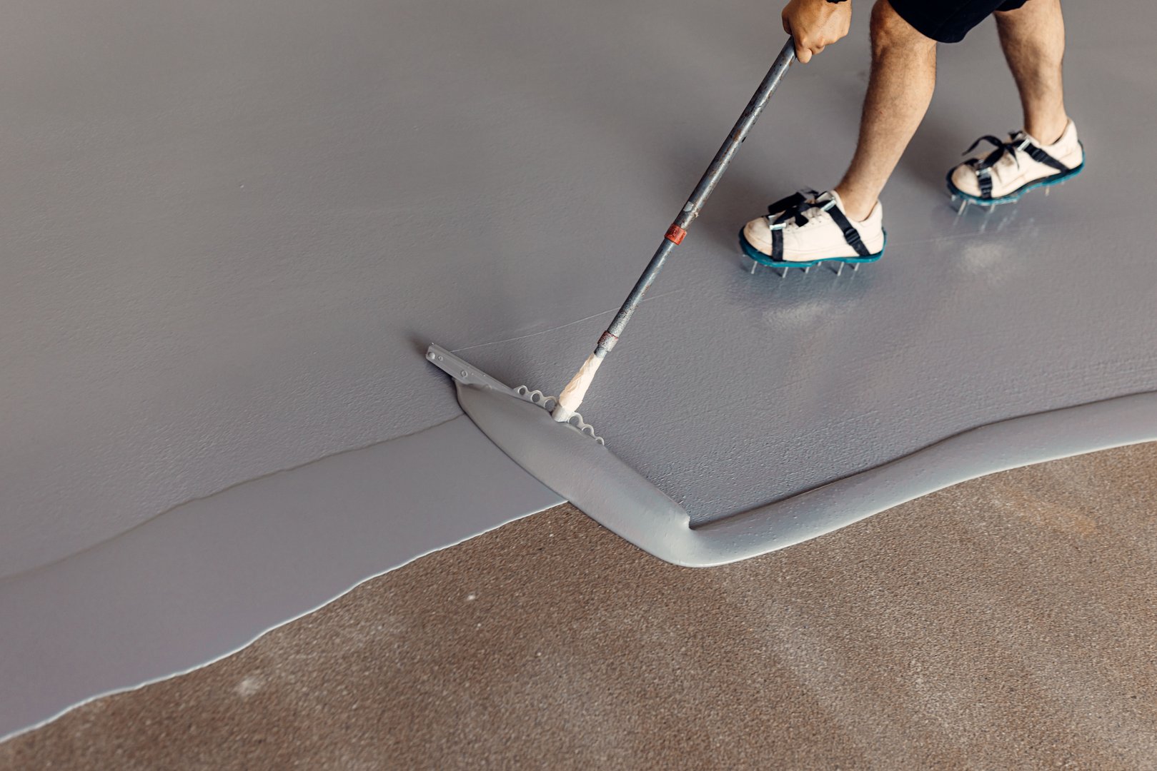 A construction worker applying grey epoxy resin in an industrial hall