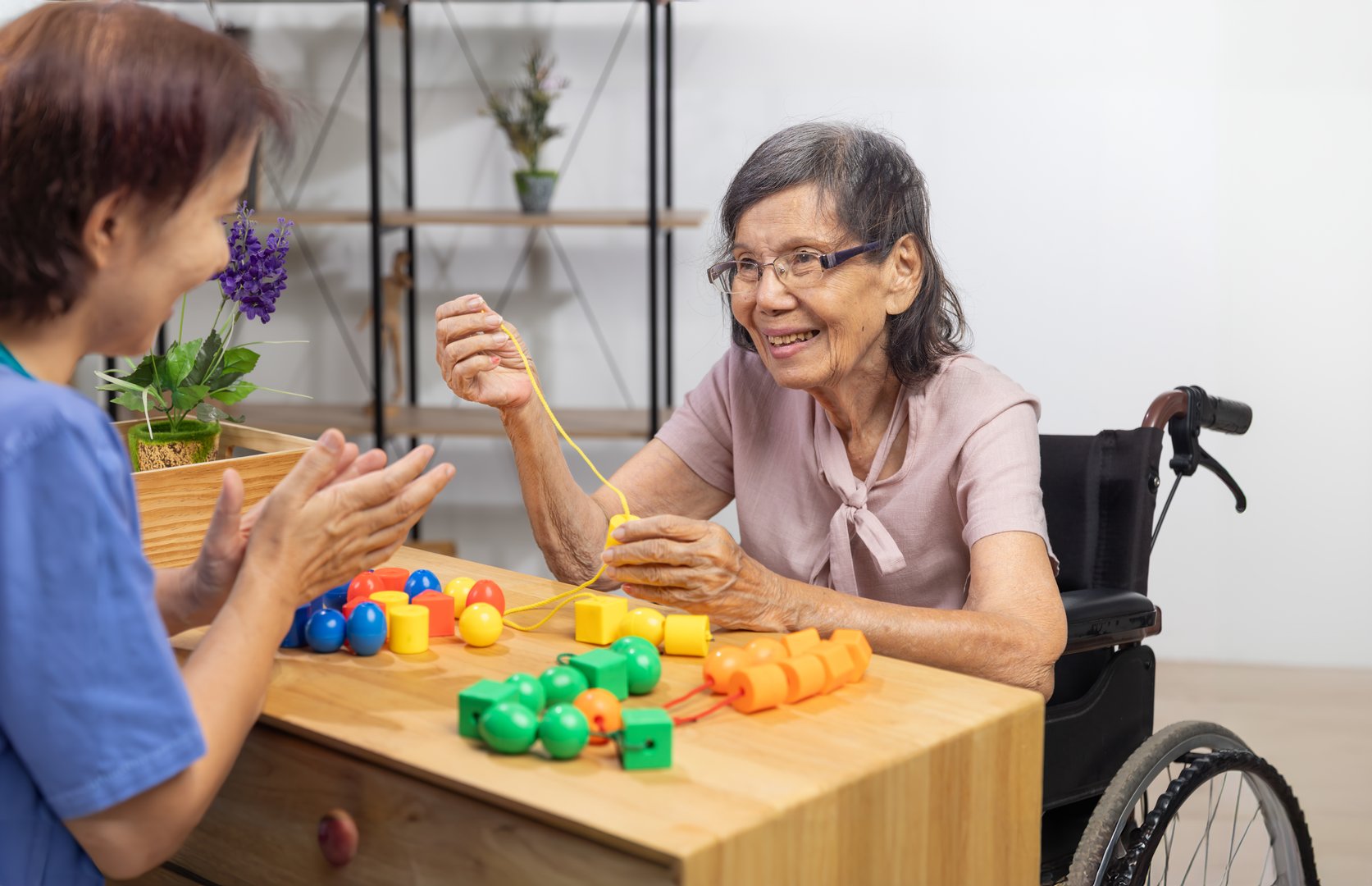 Caregiver and senior woman playing stringing beads game for dementia prevention