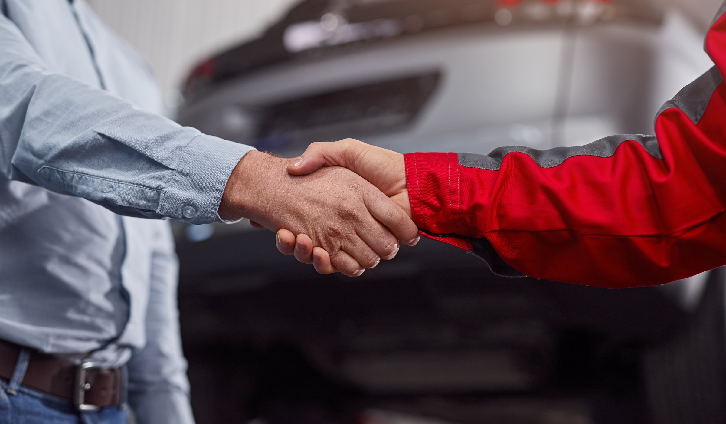 Anonymous male technician and customer shaking hands near car after coming to agreement in garage
