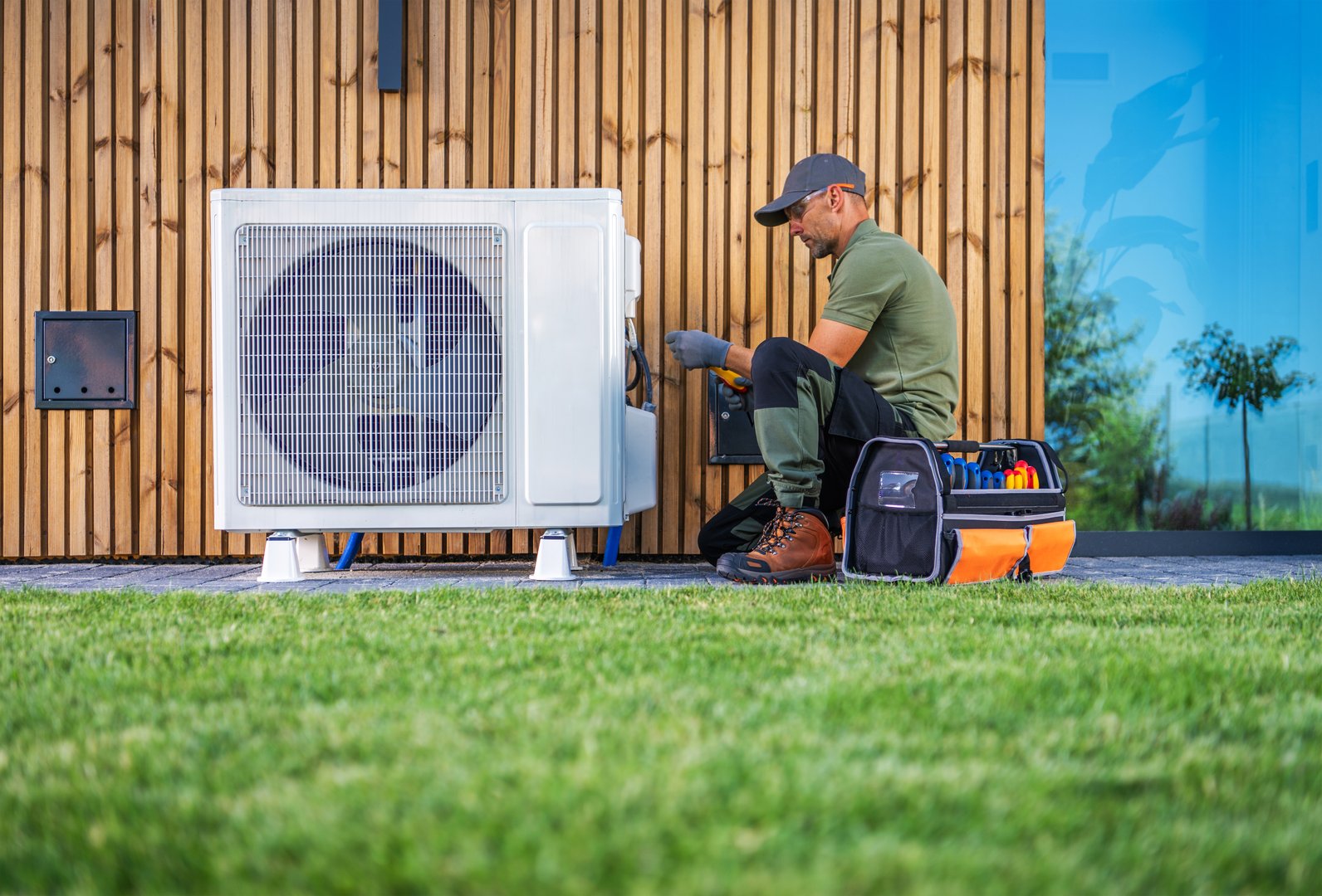 A technician servicing an air conditioning unit beside a modern home, showcasing professional repair services