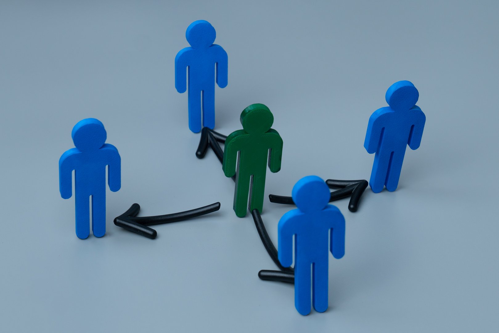 A green figure at the center surrounded by blue figures with arrows. Green figure distributes tasks or responsibilities to others. Delegation concept.
