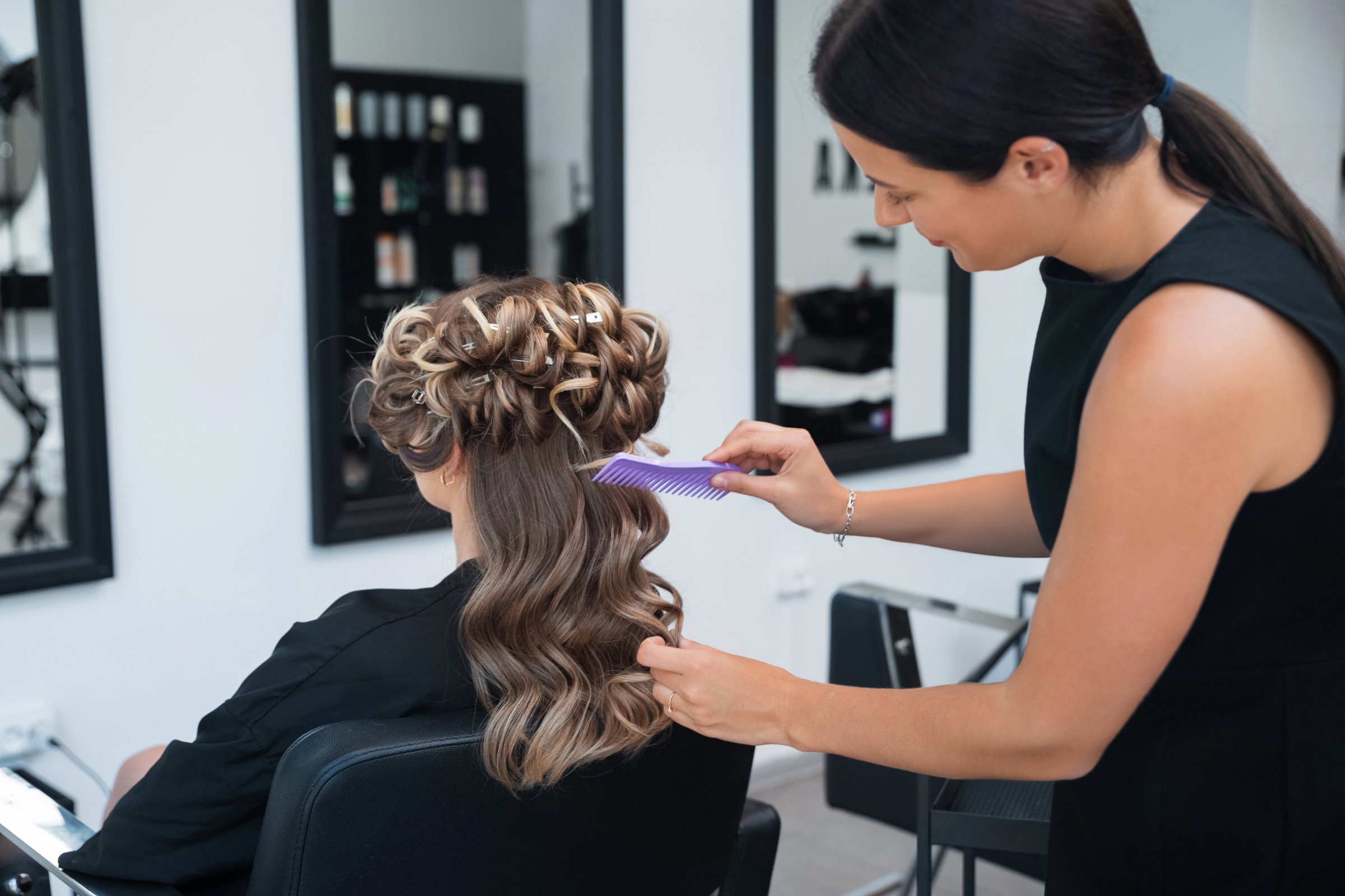 A hairstylist carefully creates a beautiful updo for a client in a contemporary salon. The atmosphere is modern, emphasizing skill and creativity in hair design.
