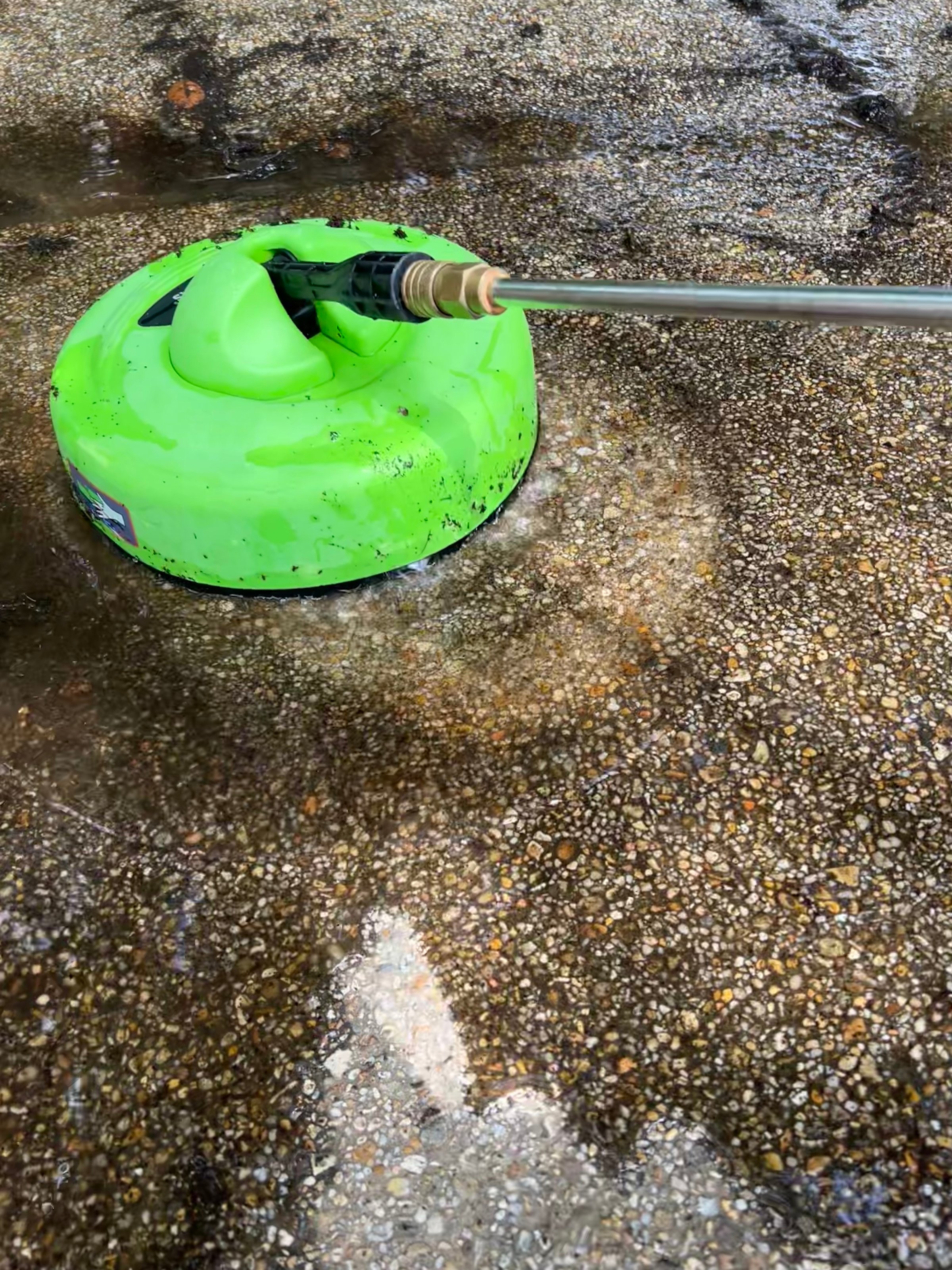 The image shows a power washer cleaning a concrete surface