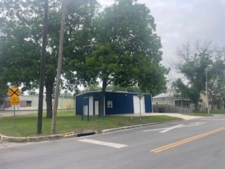Small blue building with white doors next to trees and a road, near a railroad crossing sign.