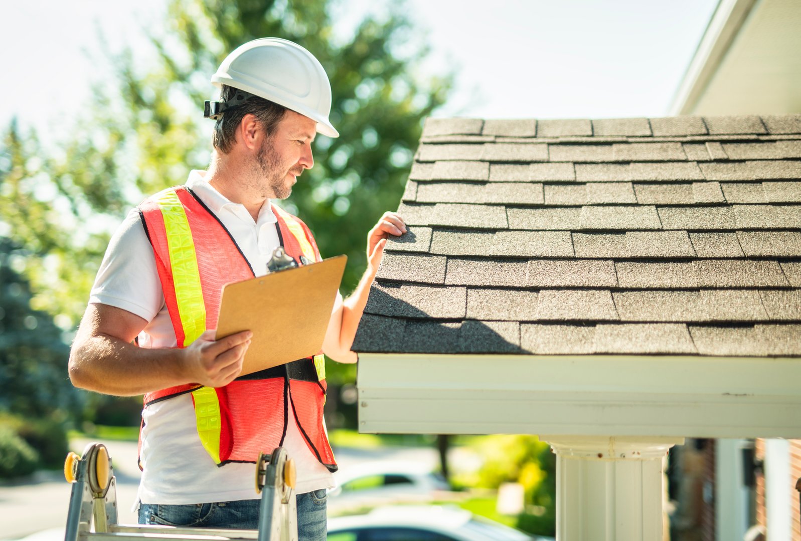 A man with hard hat standing on steps inspecting house roof