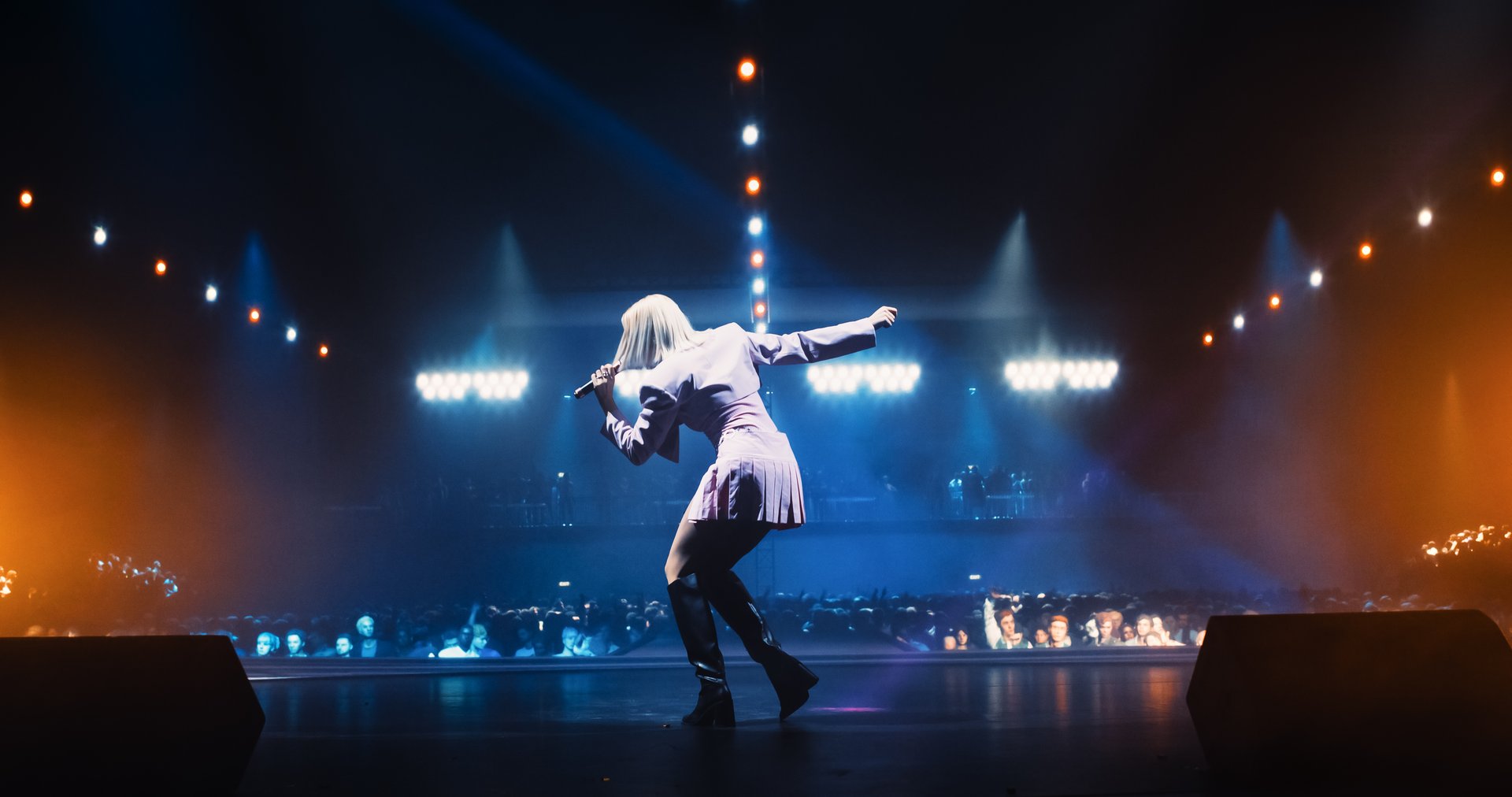 Music Contest: Back View of a Pop Music Artist Performing a Hit Song on Stage in Front of a Sold-Out Audience. Her Charismatic Stage Presence and Lyrics Electrify the Diverse Music Fans