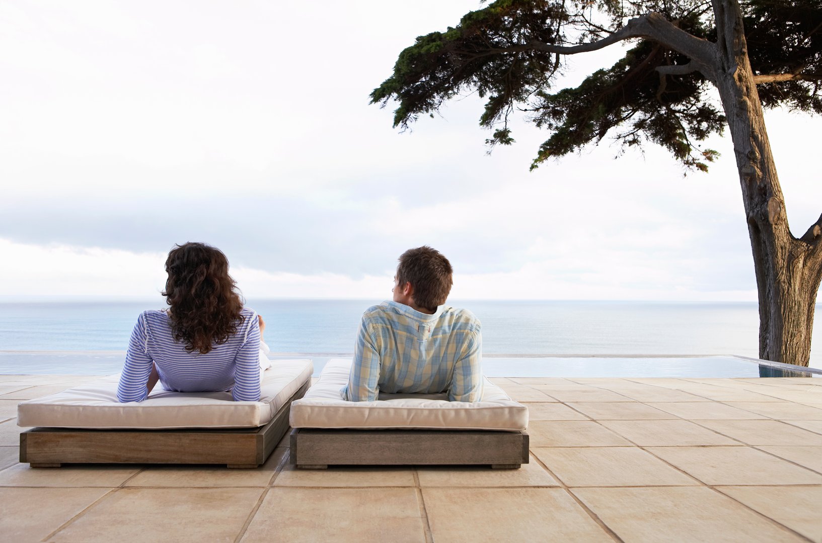 Rear view of young couple relaxing on sunbeds by infinity pool