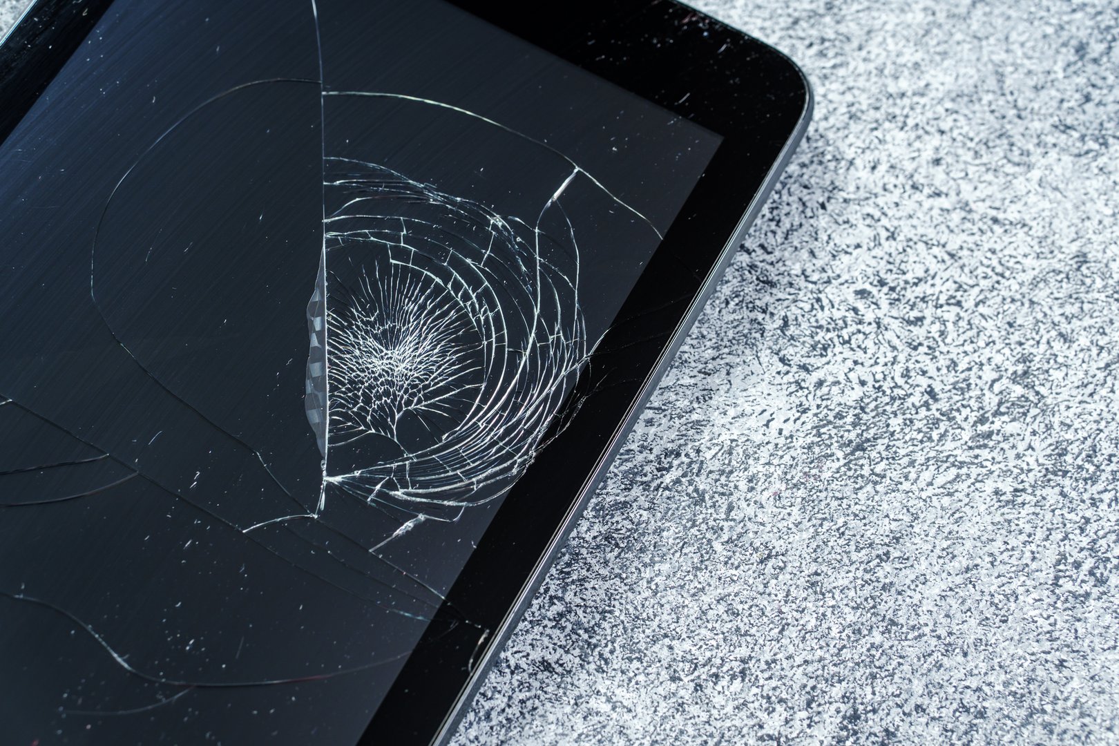 Broken tablet with a damaged screen lies on concrete, close-up