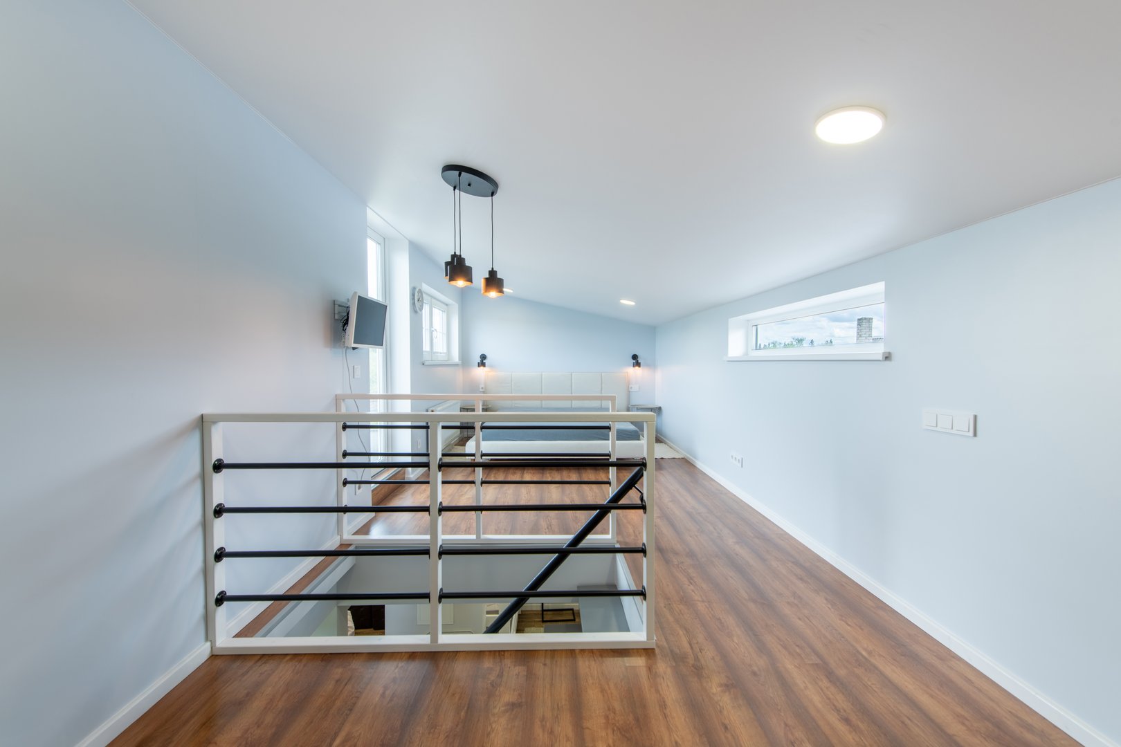 Bright and clean loft interior featuring polished wooden floors, light blue walls, and an elegant railing system, creating a contemporary and spacious ambiance.