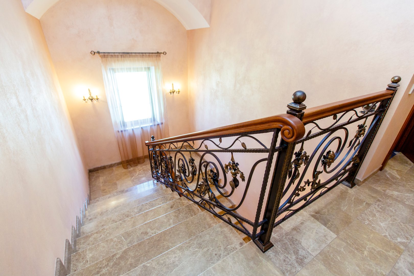 wrought iron staircase in the cottage. Marble steps, black wrought iron stairs with floral ornaments. Mahogany wooden railing.