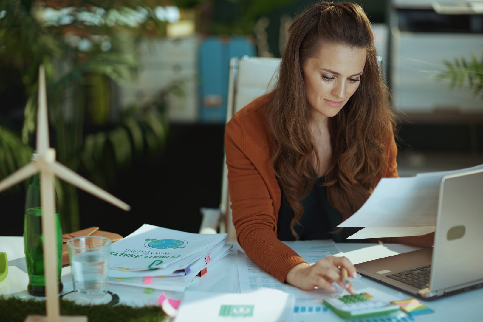 modern 40 years old small business owner woman with laptop and calculator working with documents in the modern green office.
