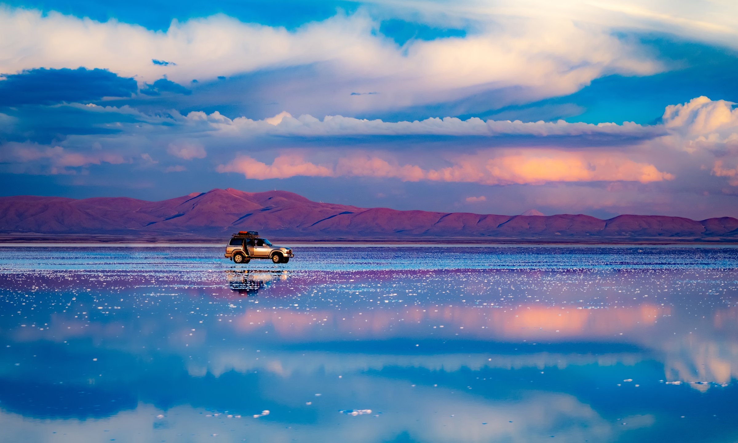 Car standing in middle of salt flat reflecting blue sky, Salar de Uyuni, Bolivia