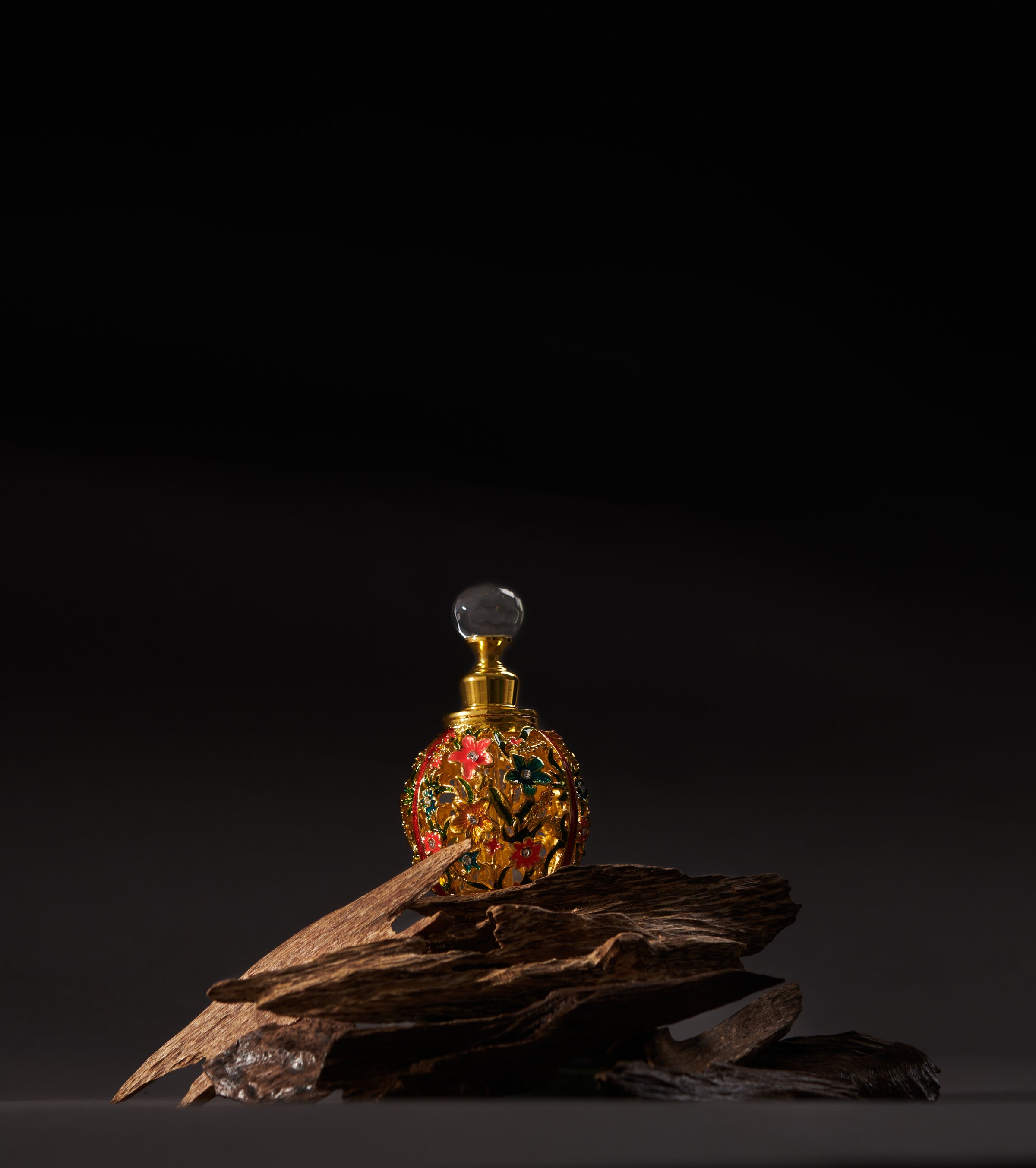 A bottle of agarwood perfume with pieces of agarwood on a dark background