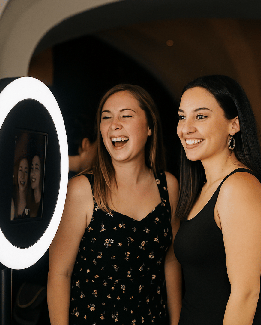 Two women smiling and posing in front of a photo booth with a circular ring light.