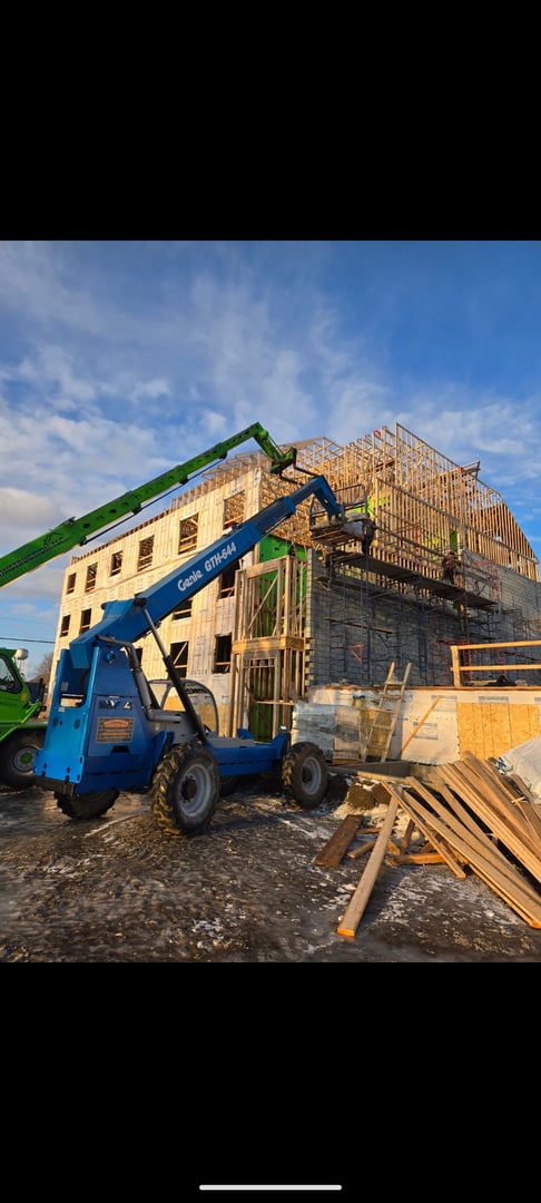 Construction site with a building under progress, featuring scaffolding and a blue forklift in the foreground.