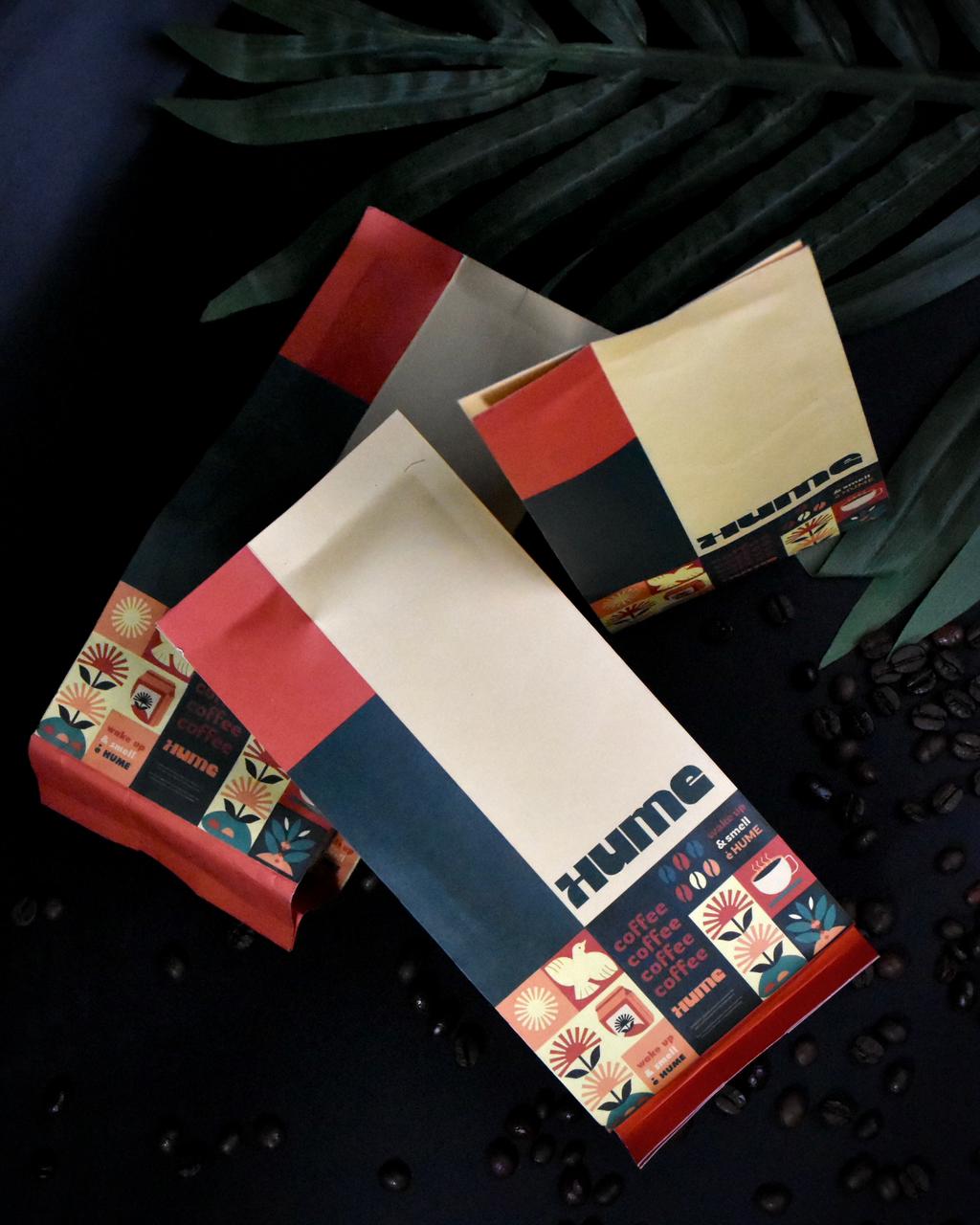 Three decorative coffee bags with colorful patterns on a dark background, surrounded by scattered coffee beans.