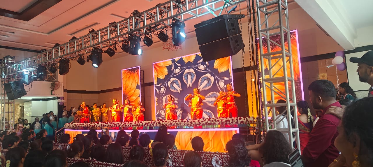 Dance troupe in vibrant costumes performing on a decorated stage with an audience watching.