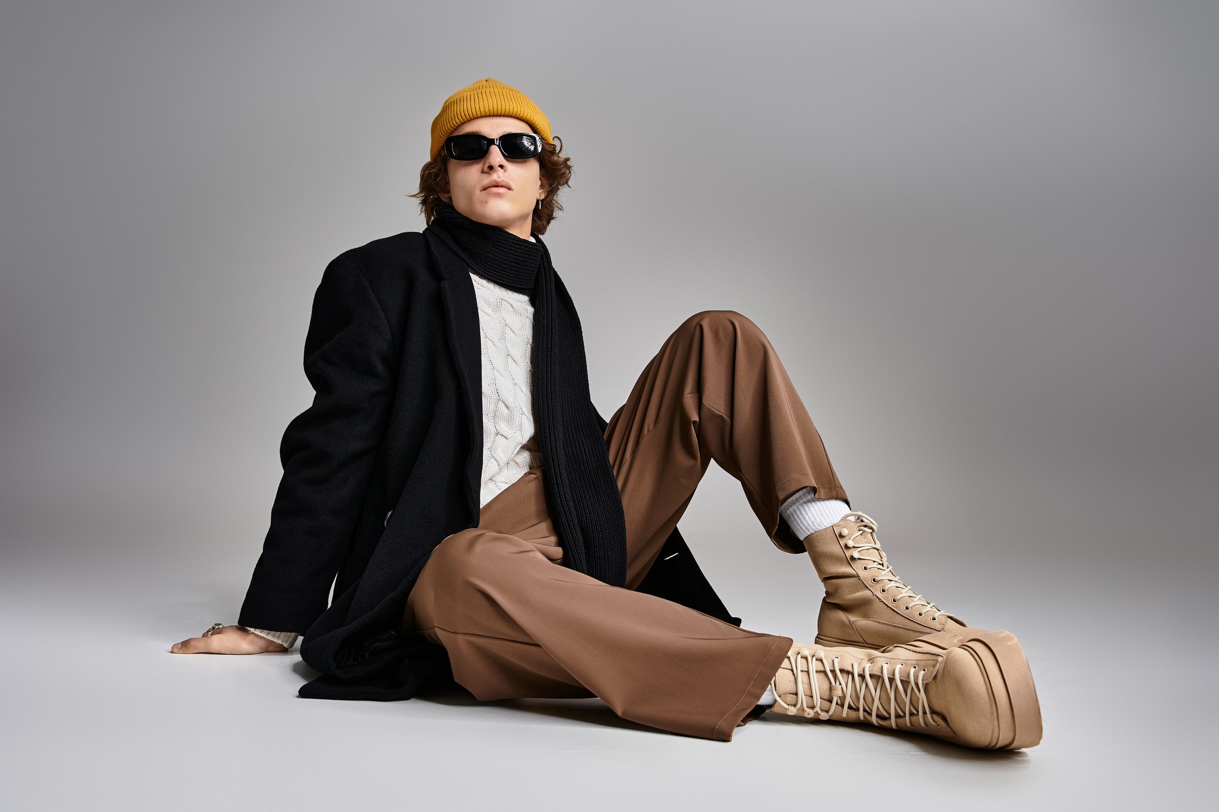 This young man exudes charisma in a trendy black coat and a bold yellow beanie, relaxed in a studio.