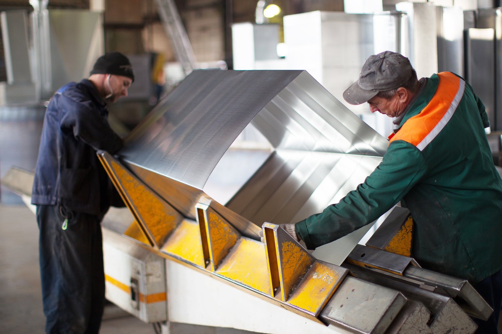 Two workers make metal ventilation pipes in the workshop at the factory