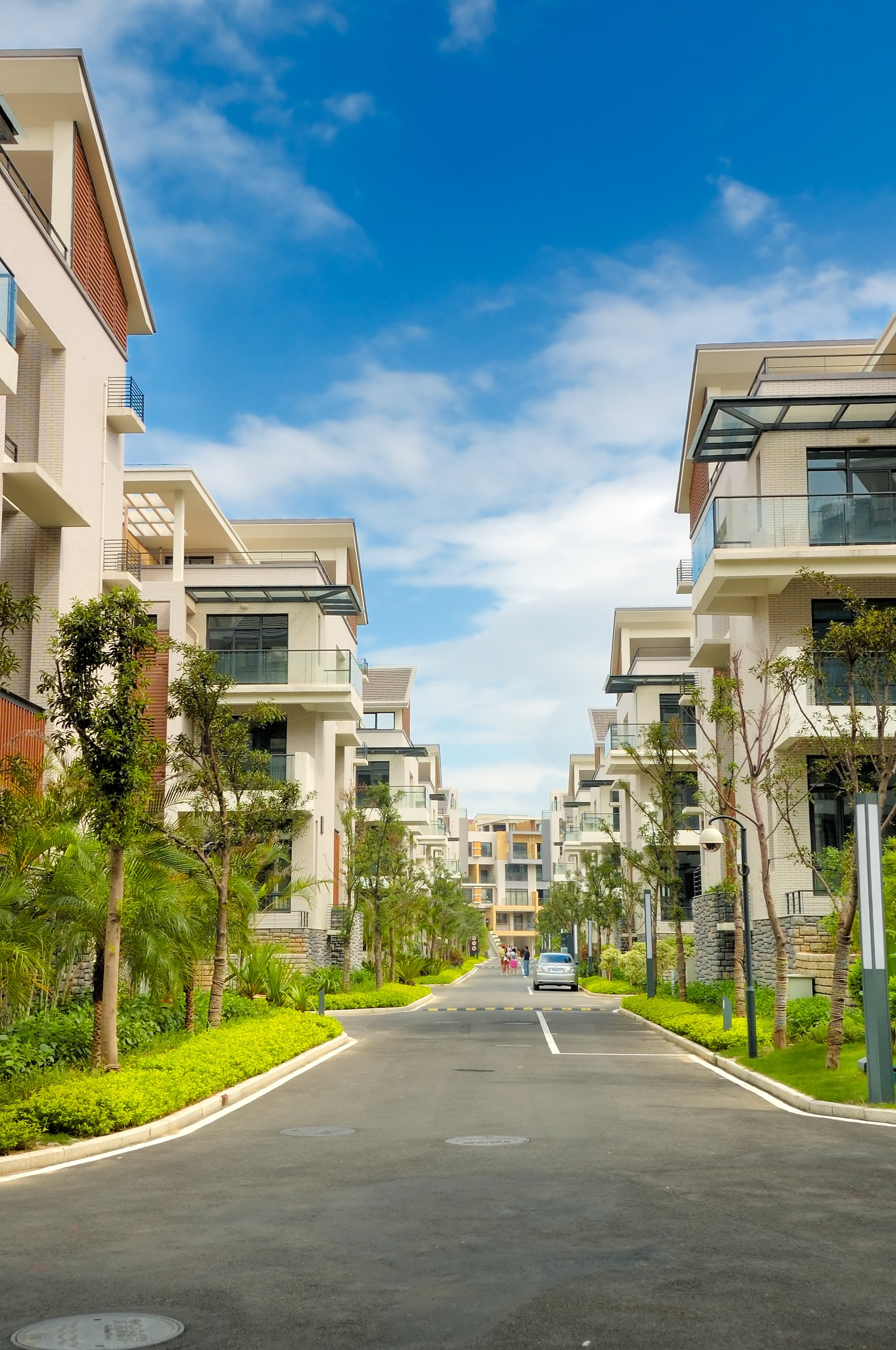 A symmetrical view of a residential street lined with modern apartment buildings and lush greenery under a clear blue sky.