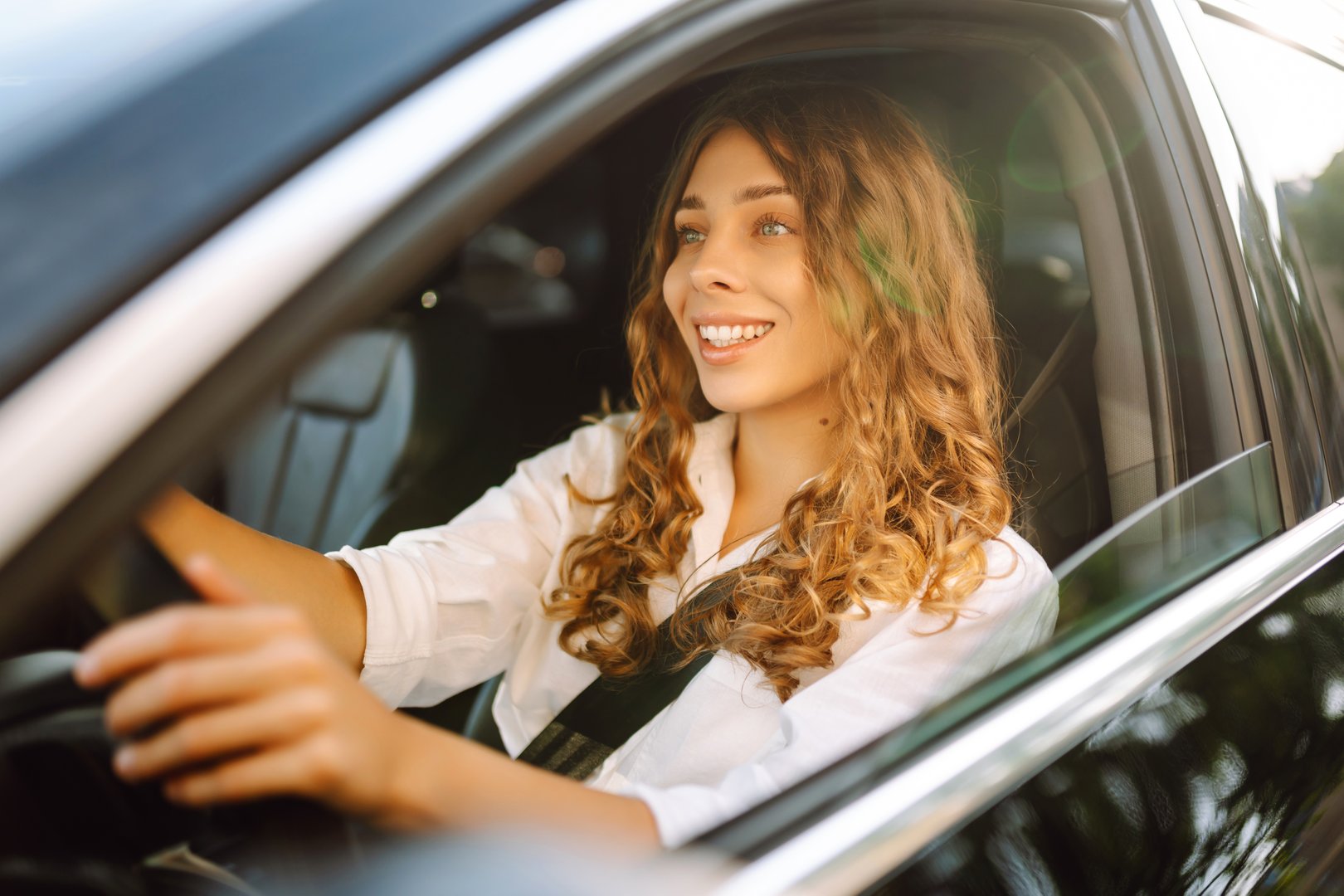 Portrait of smiling woman sitting behind the wheel of car looking out the window. Woman driver in modern car enjoying sunny day. Transport, taxi concept. Lifestyle.