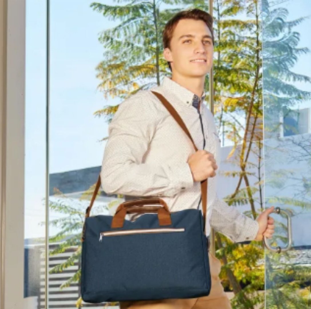 A man in a suit stands outdoors holding a red umbrella, with greenery and a building in the background.